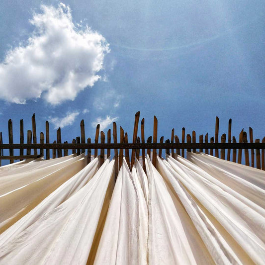 a 2 point perspective shot from below of Kora Khadi fabric hang drying in the sun under a clear blue sky. The picture a slight flare and a small clour in top left half.