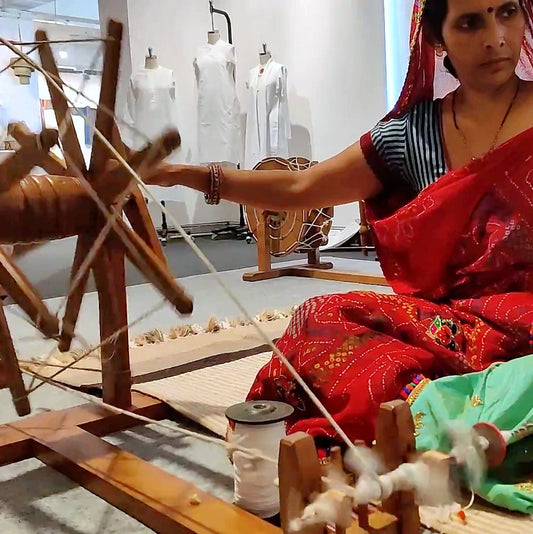 A Rajasthani women clad in bandhini saree sitting on ground and spinning cotton yarn (soot) on a Gandhi Charkha (Indian Spinning Wheel)