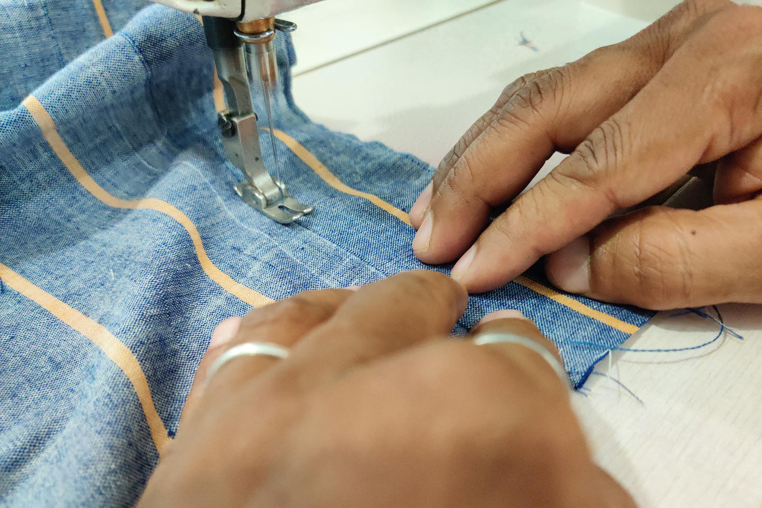 a close of hands of tailor on sewing maching stitching blue handspun cotton Khadi fabric by Cotton Rack.