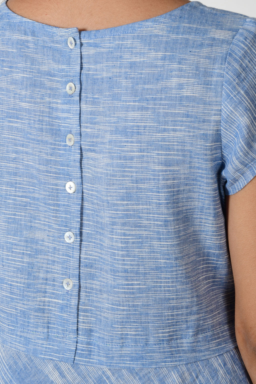 close up of mother of pearl buttons on the back of a space dyed blue cotton dress.