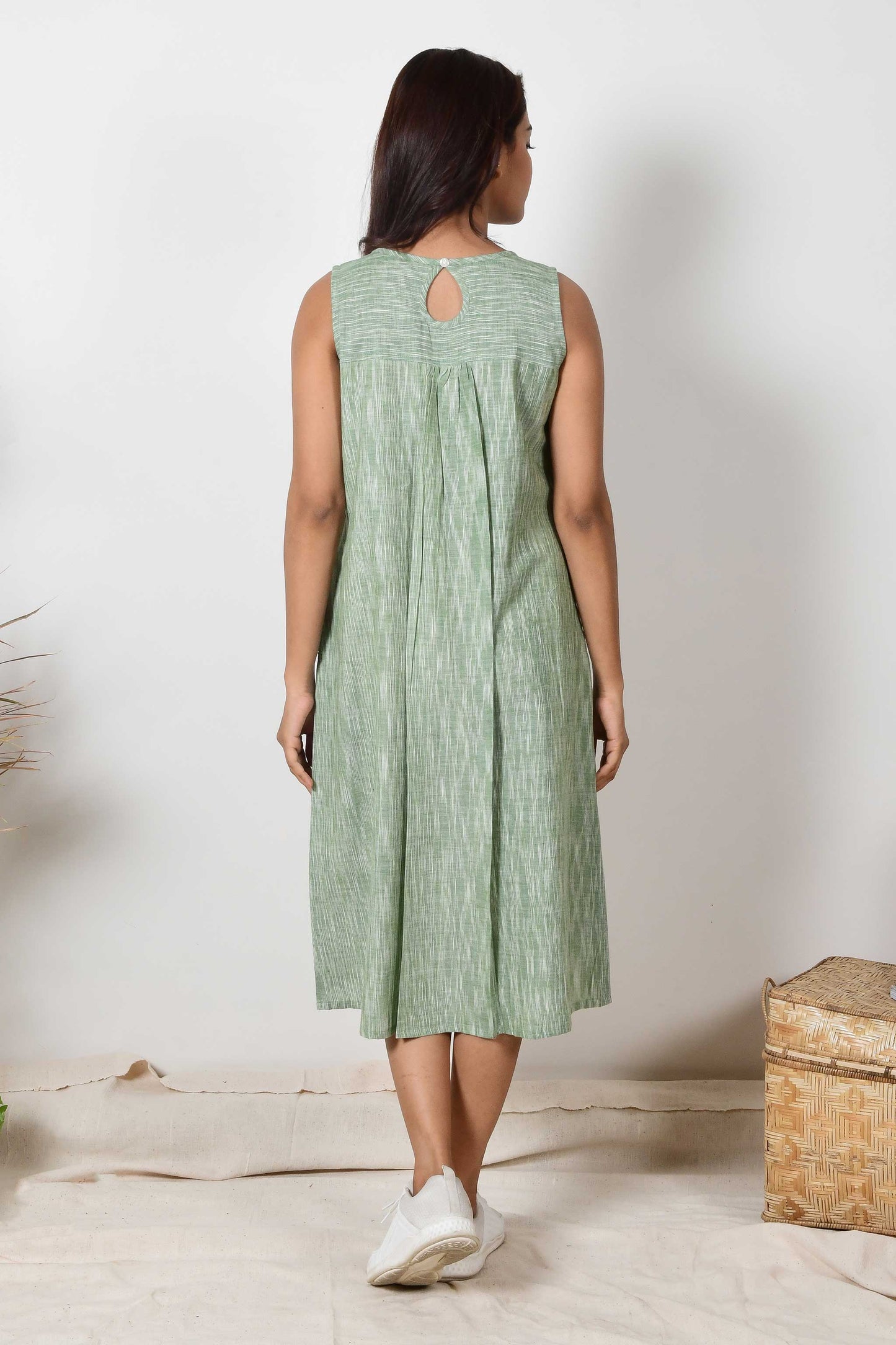 back of a dark haired Indian girl wearing a handspun cotton green sleeveless pleated dress.a