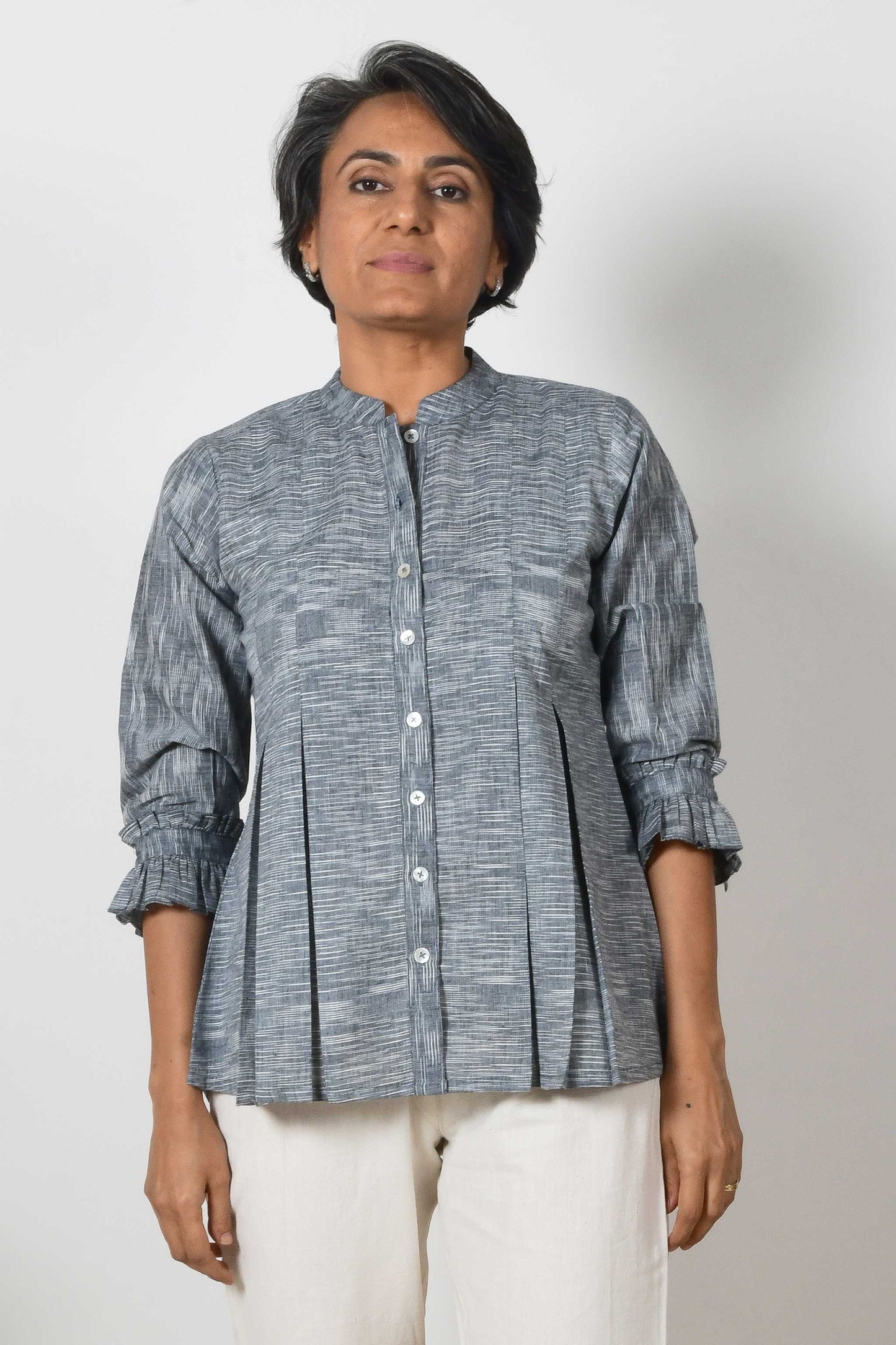 Smiling woman with beautiful short grey hair wearing offwhite cotton pants and black cotton shirt blouse with texture on the fabric and box pleats on the top.