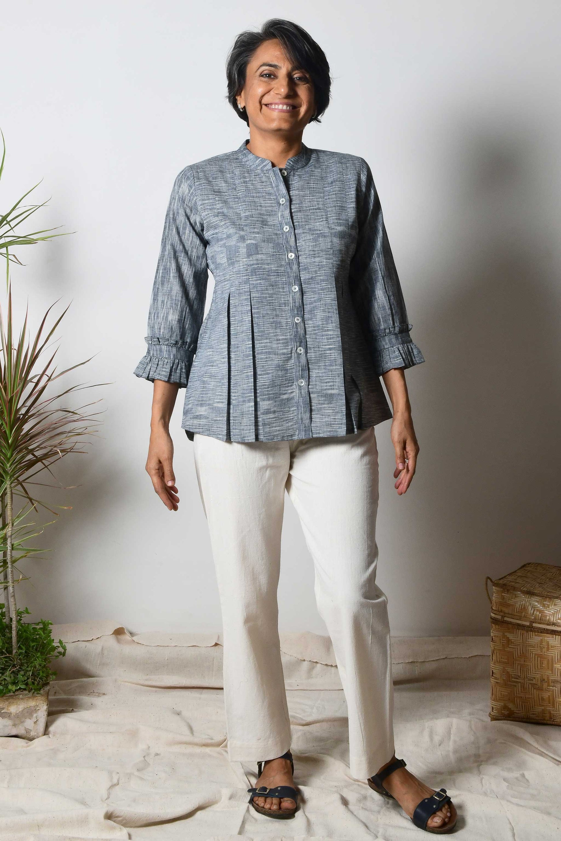 Smiling woman with beautiful short grey hair wearing offwhite cotton pants and black cotton shirt blouse with texture on the fabric and box pleats on the top.