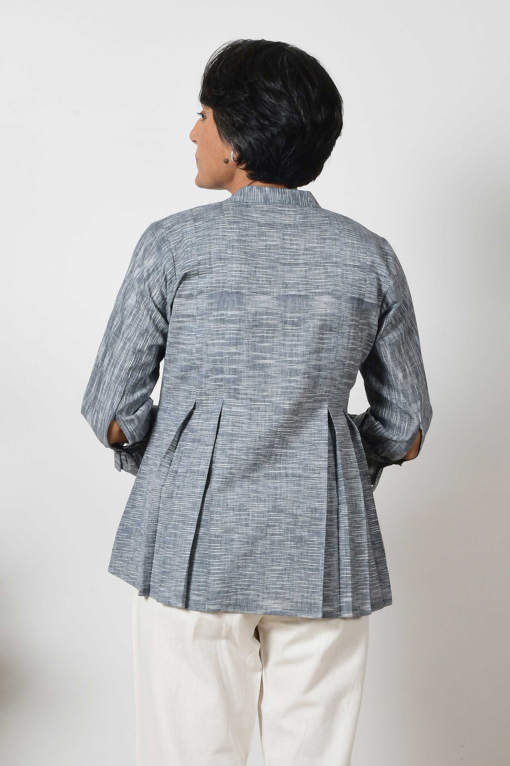 back close up of the short haired indian woman wearing a black textured cotton top with box pleat details.
