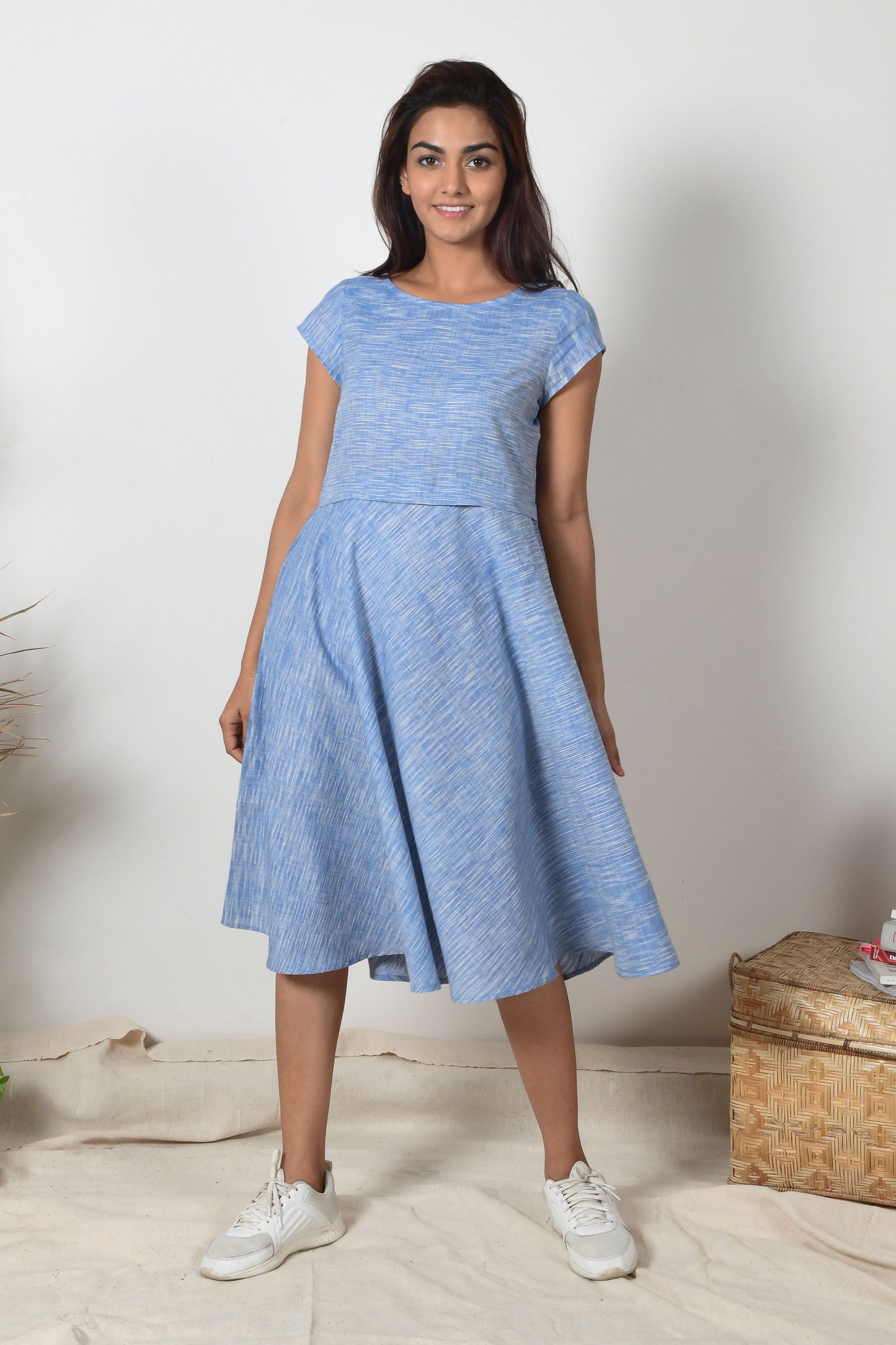 Indian girl with black hair and white sneakers wearing a blue a-line dress made with cotton that hand spun and hand woven.