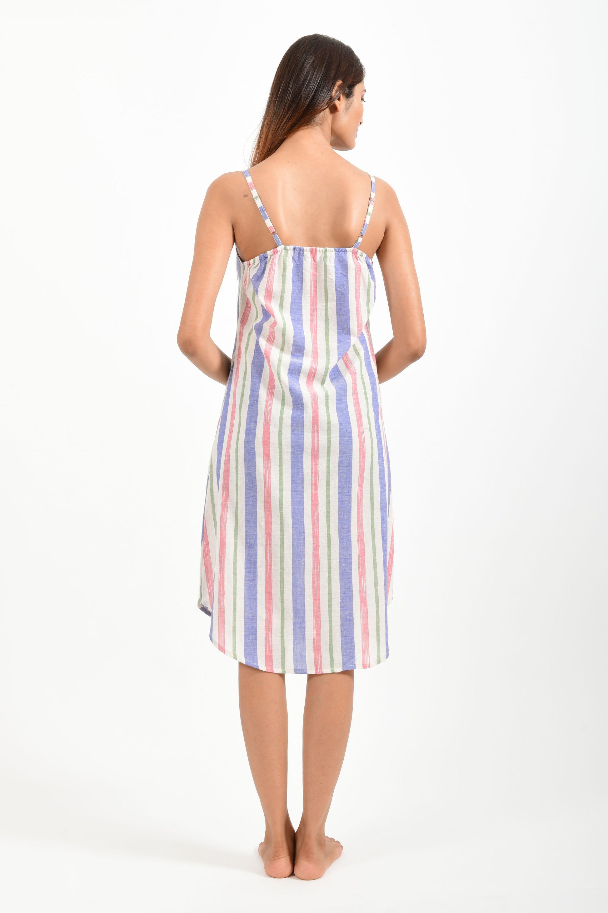 Back pose of an Indian female womenswear fashion model in an mutli colored striped handspun and handwoven khadi cotton spaghetti dress by Cotton Rack.