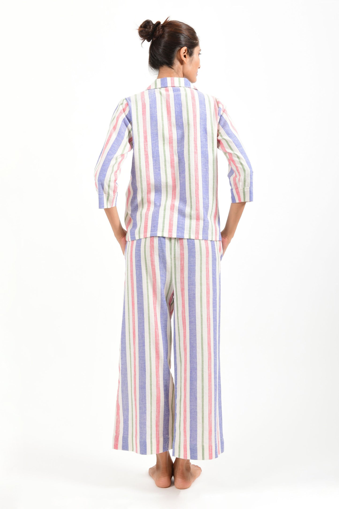 Back pose of an Indian female womenswear fashion model in a candy colored striped azo-free dyed handspun and handwoven khadi cotton nightwear pyjama & shirt by Cotton Rack.