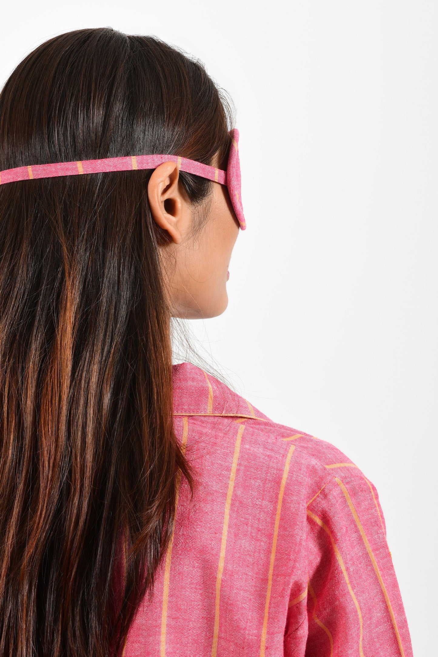 Back portrait of an Indian female womenswear fashion model wearing a red with orange stripe chambray handspun and handwoven khadi cotton eye mask by Cotton Rack.