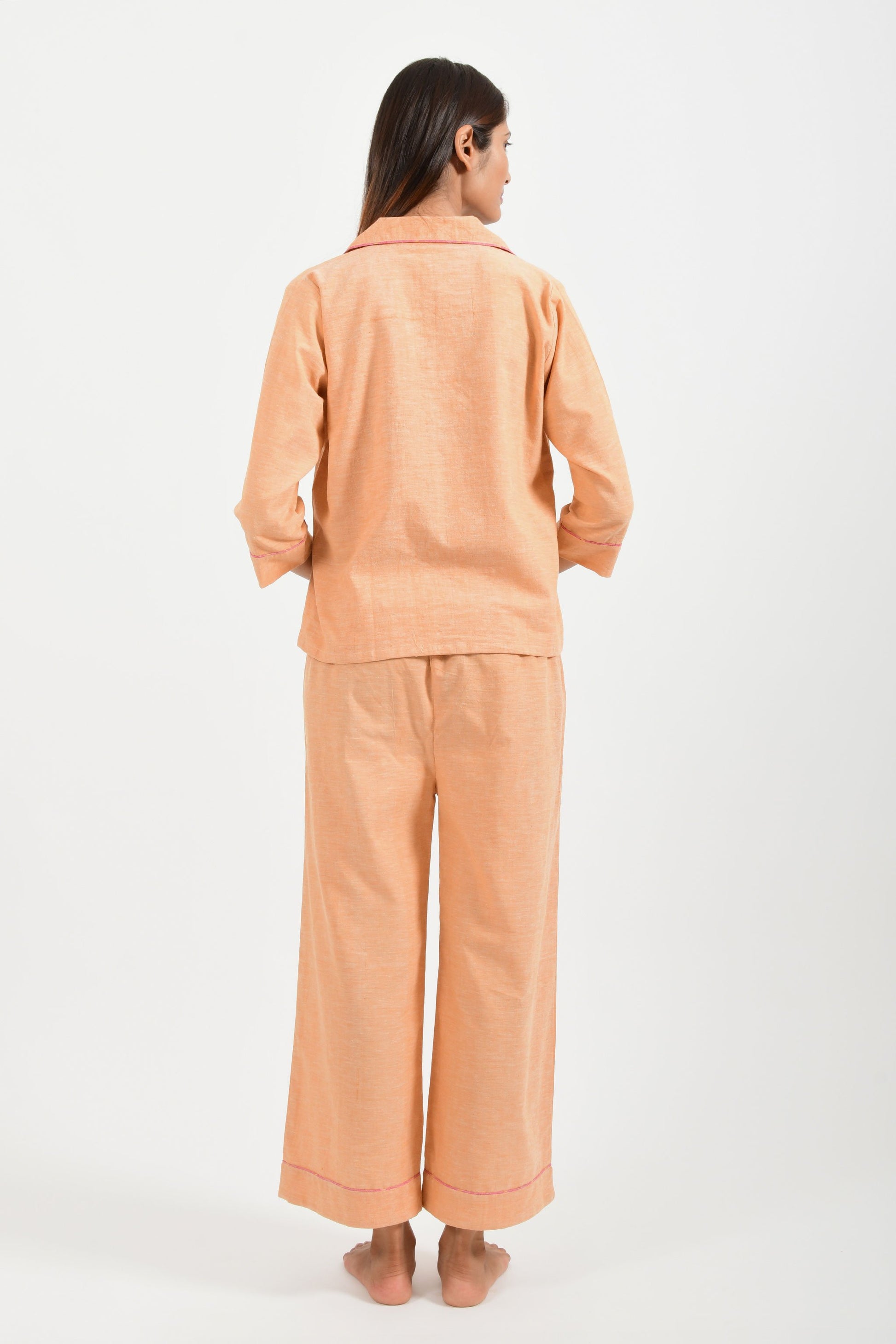 Back pose of an Indian female womenswear fashion model in azo-free dyed handspun and handwoven khadi cotton nightwear pyjama & shirt in orange chambray by Cotton Rack.