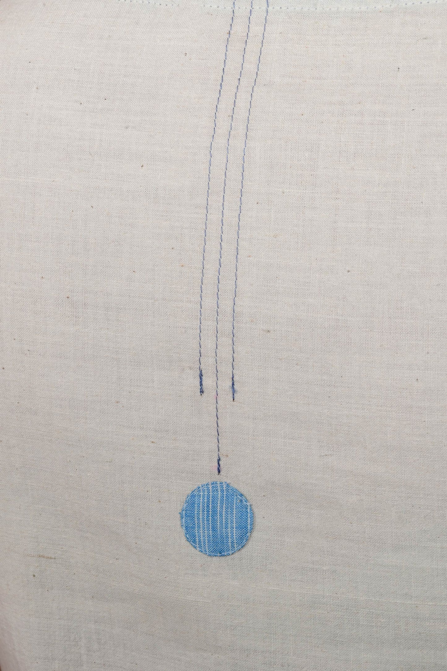close up of a stitch detail and a blue circular patch on an off white cotton fabric base.