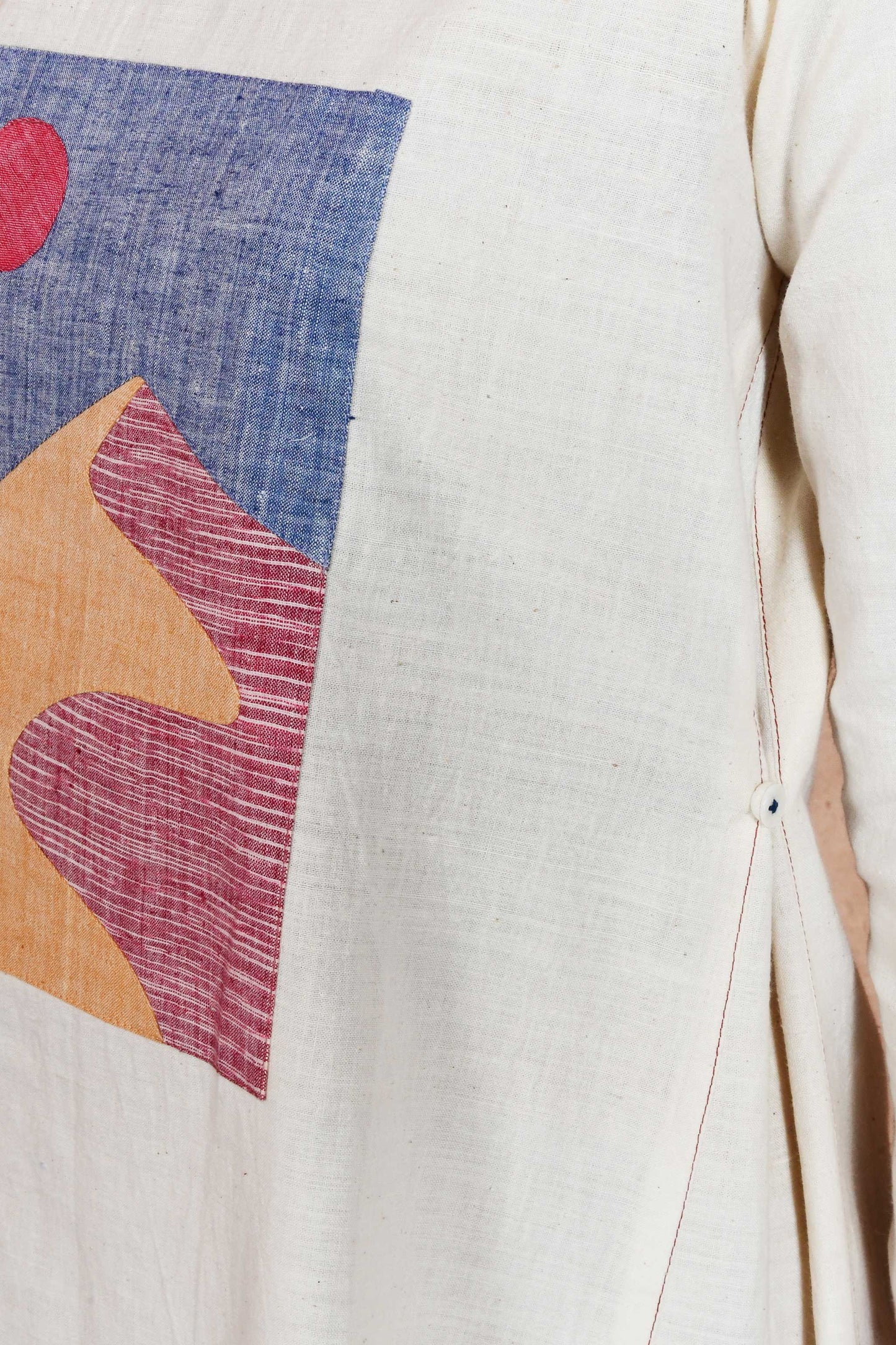 Close of an applique patch depicting sand dunes and sun and side seam detail of an off white dress.