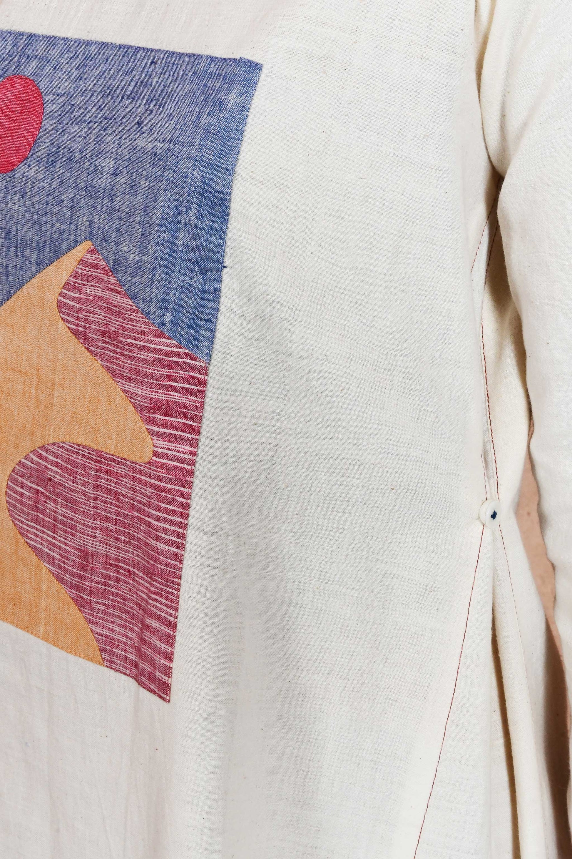 Close of an applique patch depicting sand dunes and sun and side seam detail of an off white dress.