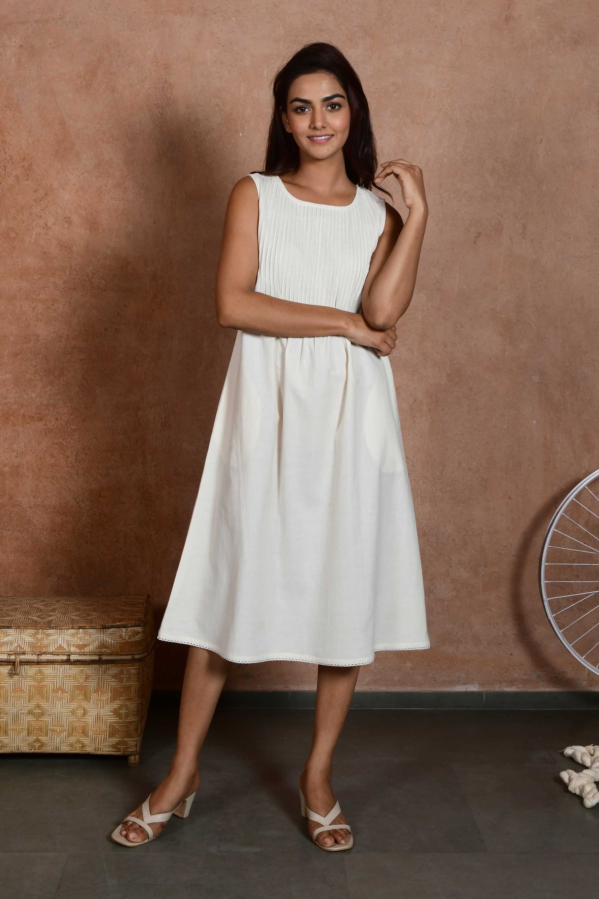 Front pose of a young indian model wearing an off white knee length a line dress with pleats till waist.