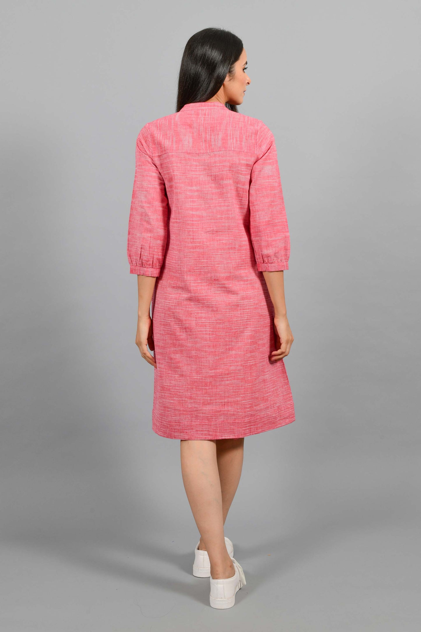 Back pose of an Indian female womenswear fashion model in a red space dyed handspun and handwoven khadi cotton dress with collar and ruffles on front placket by Cotton Rack.