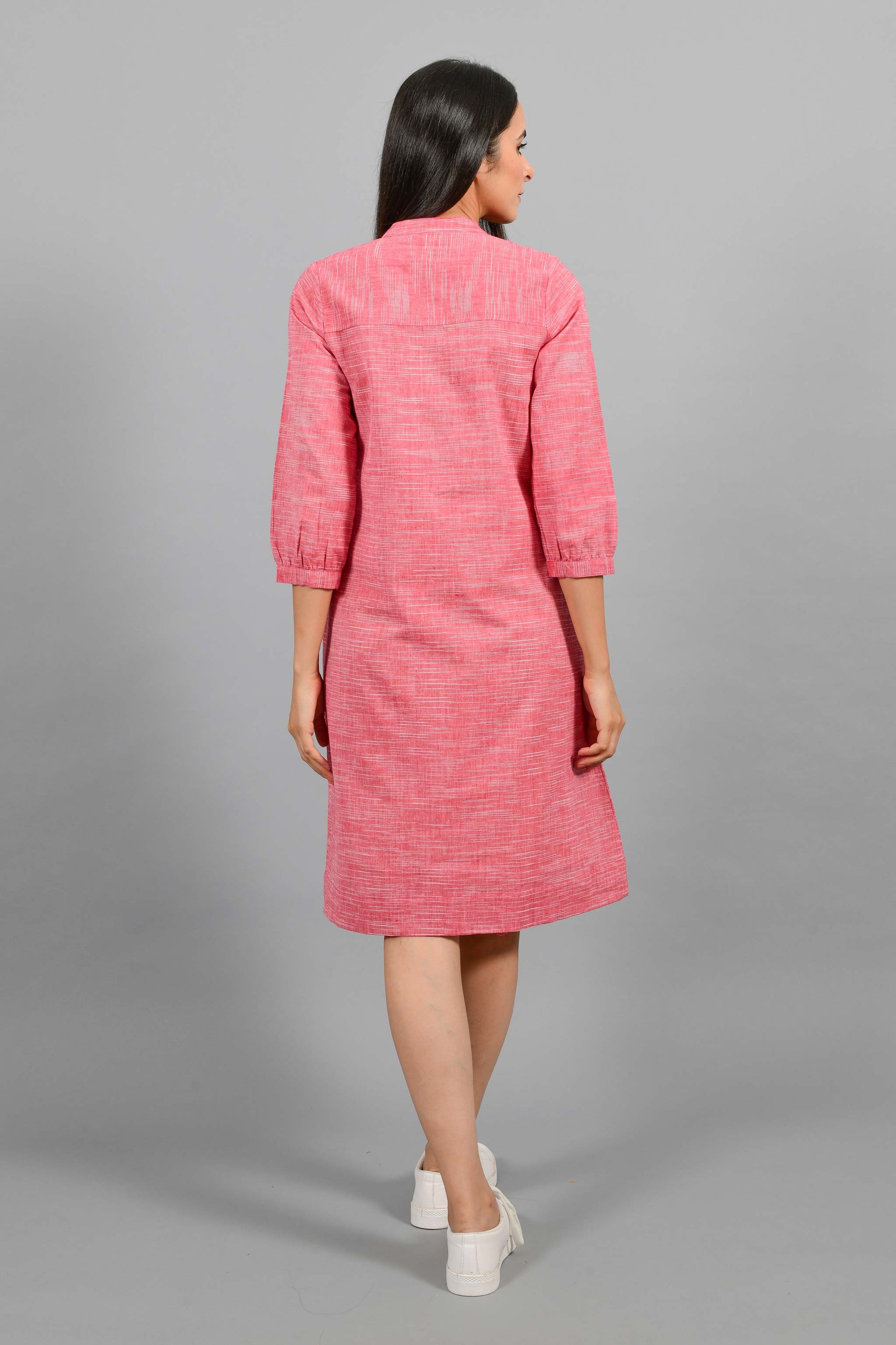 Back pose of an Indian female womenswear fashion model in a red space dyed handspun and handwoven khadi cotton dress with collar and ruffles on front placket by Cotton Rack.