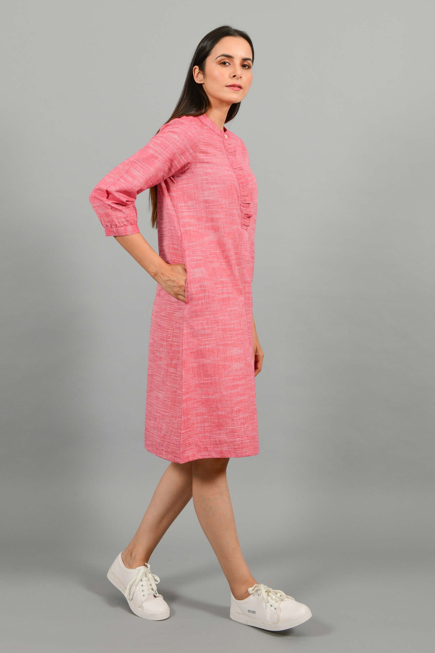 Side walking pose of an Indian female womenswear fashion model in a red space dyed handspun and handwoven khadi cotton dress with collar and ruffles on front placket by Cotton Rack.