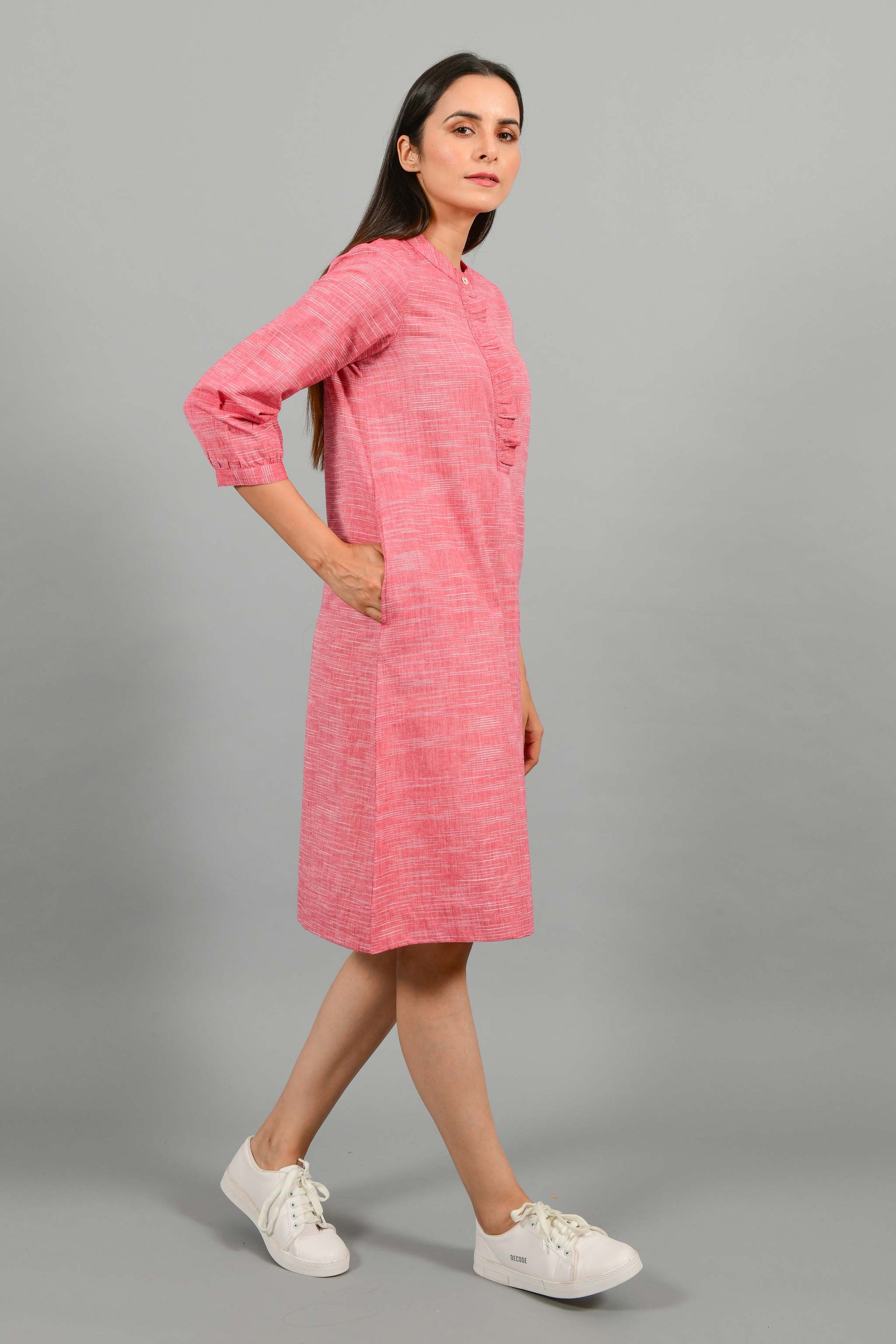 Side walking pose of an Indian female womenswear fashion model in a red space dyed handspun and handwoven khadi cotton dress with collar and ruffles on front placket by Cotton Rack.