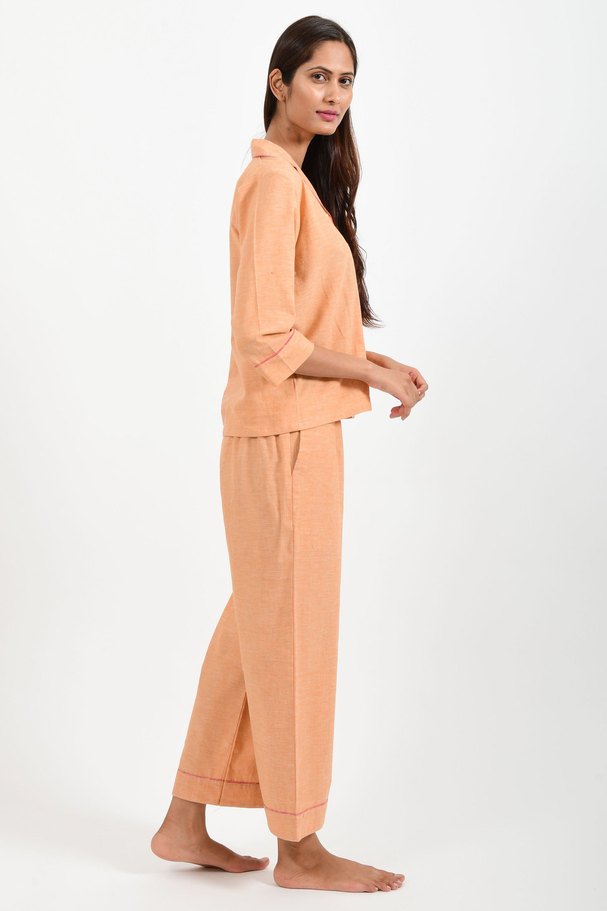 Side pose of an Indian female womenswear fashion model in azo-free dyed handspun and handwoven khadi cotton nightwear pyjama & shirt in orange chambray by Cotton Rack.