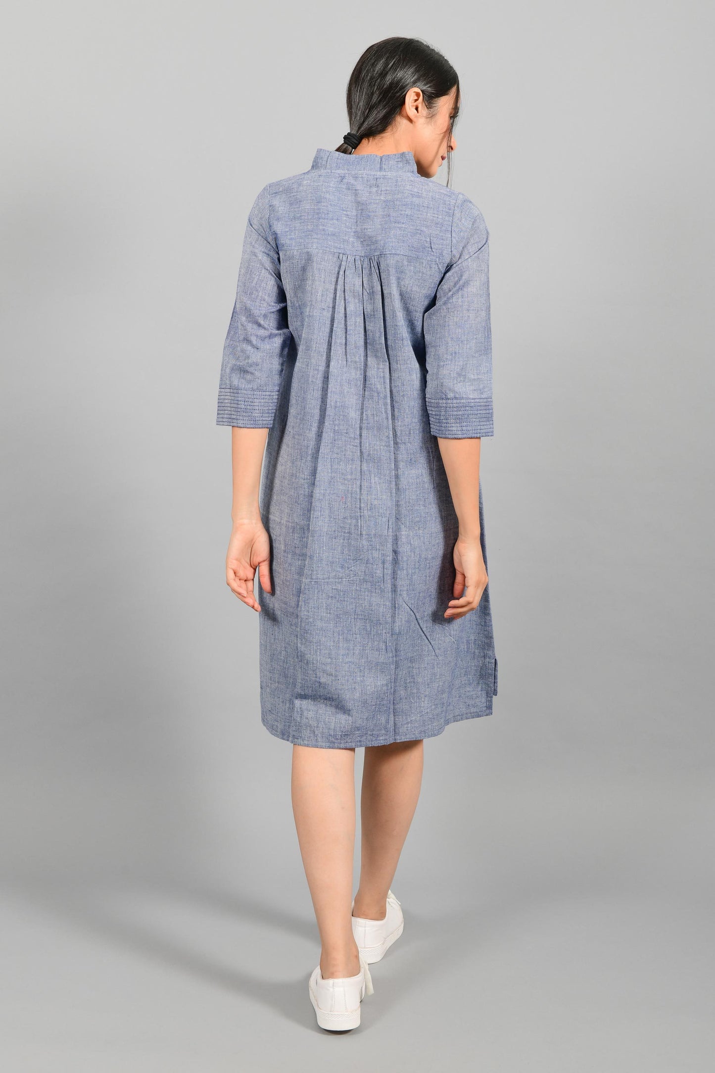 Back pose of an Indian female womenswear fashion model in a blue chambray handspun and handwoven khadi cotton dress-kurta by Cotton Rack.