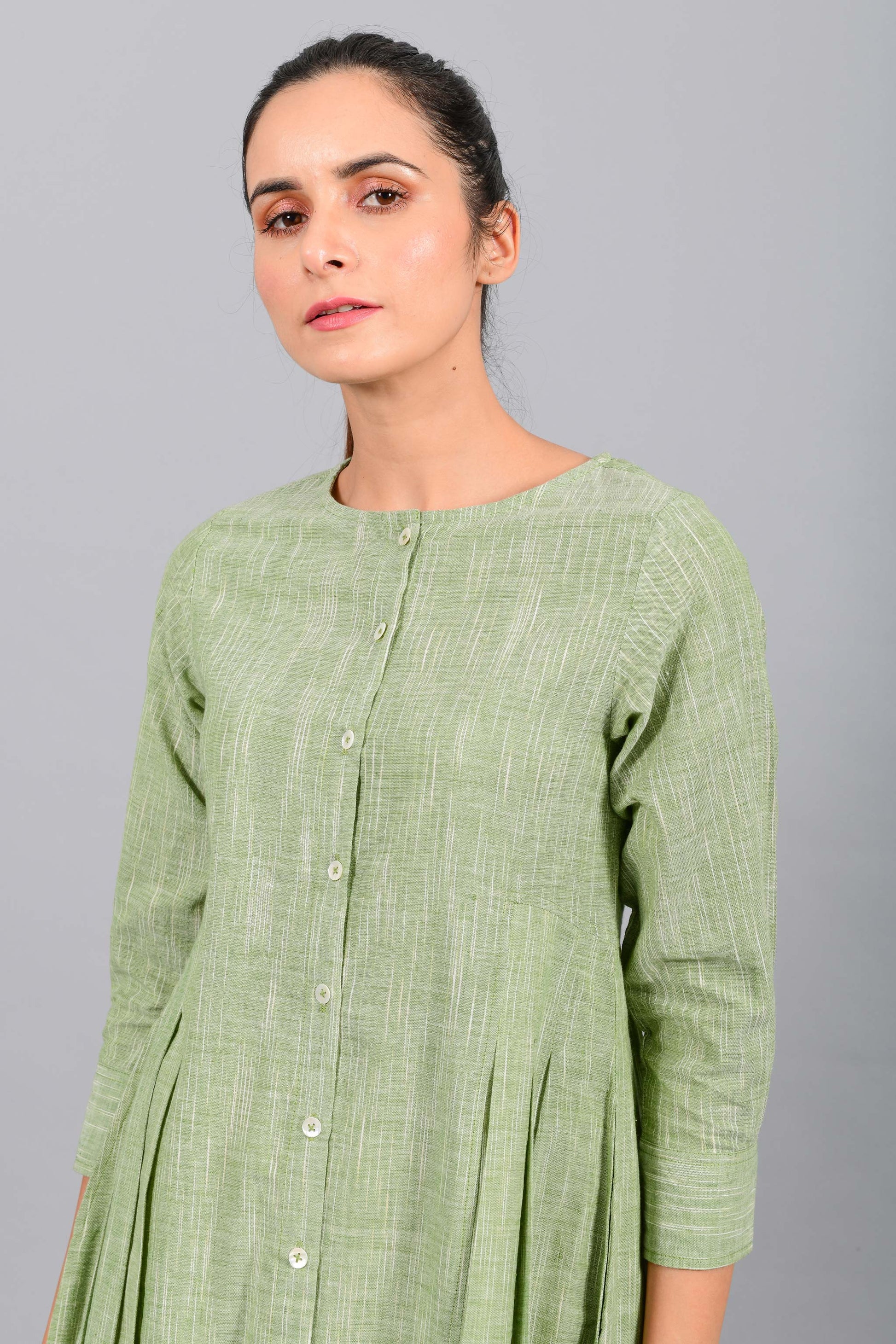 Close up portrait of an Indian female womenswear fashion model in a space dyed olive green handspun and handwoven khadi cotton pleated dress-kurta by Cotton Rack.