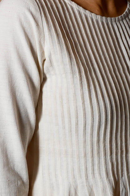 Close up of the knife pleats on the front of an off white dress.