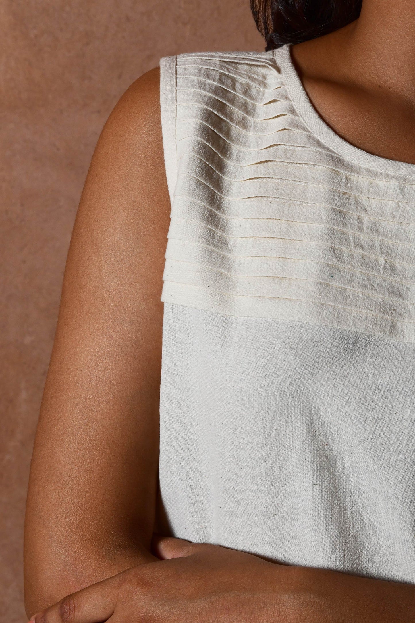 Front closeup of young Indian model posing wearing off white sleeveless pleated top.