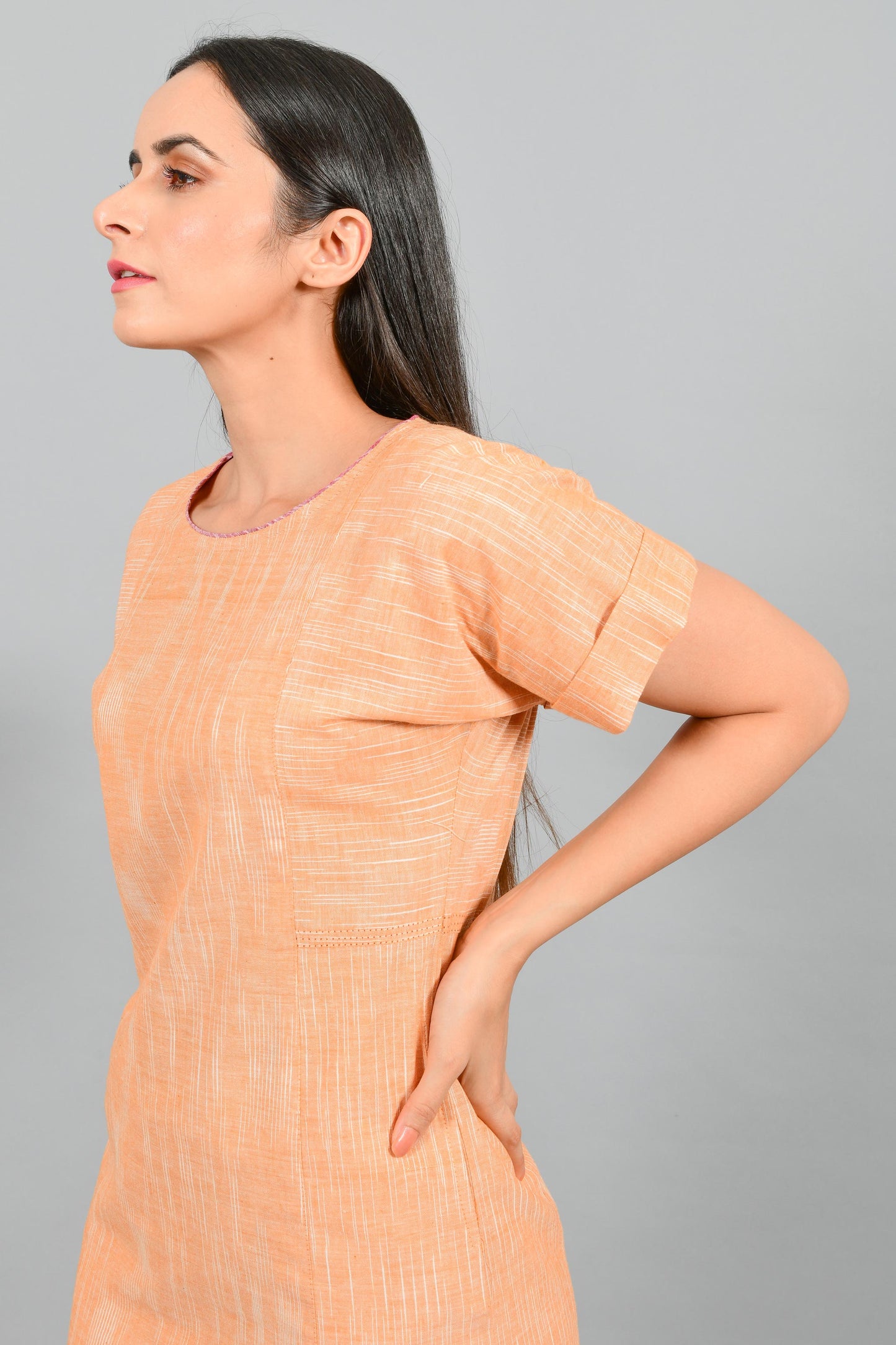 Side close up portrait of an Indian female womenswear fashion model in an orange space dyed handspun and handwoven khadi cotton panelled dress by Cotton Rack.