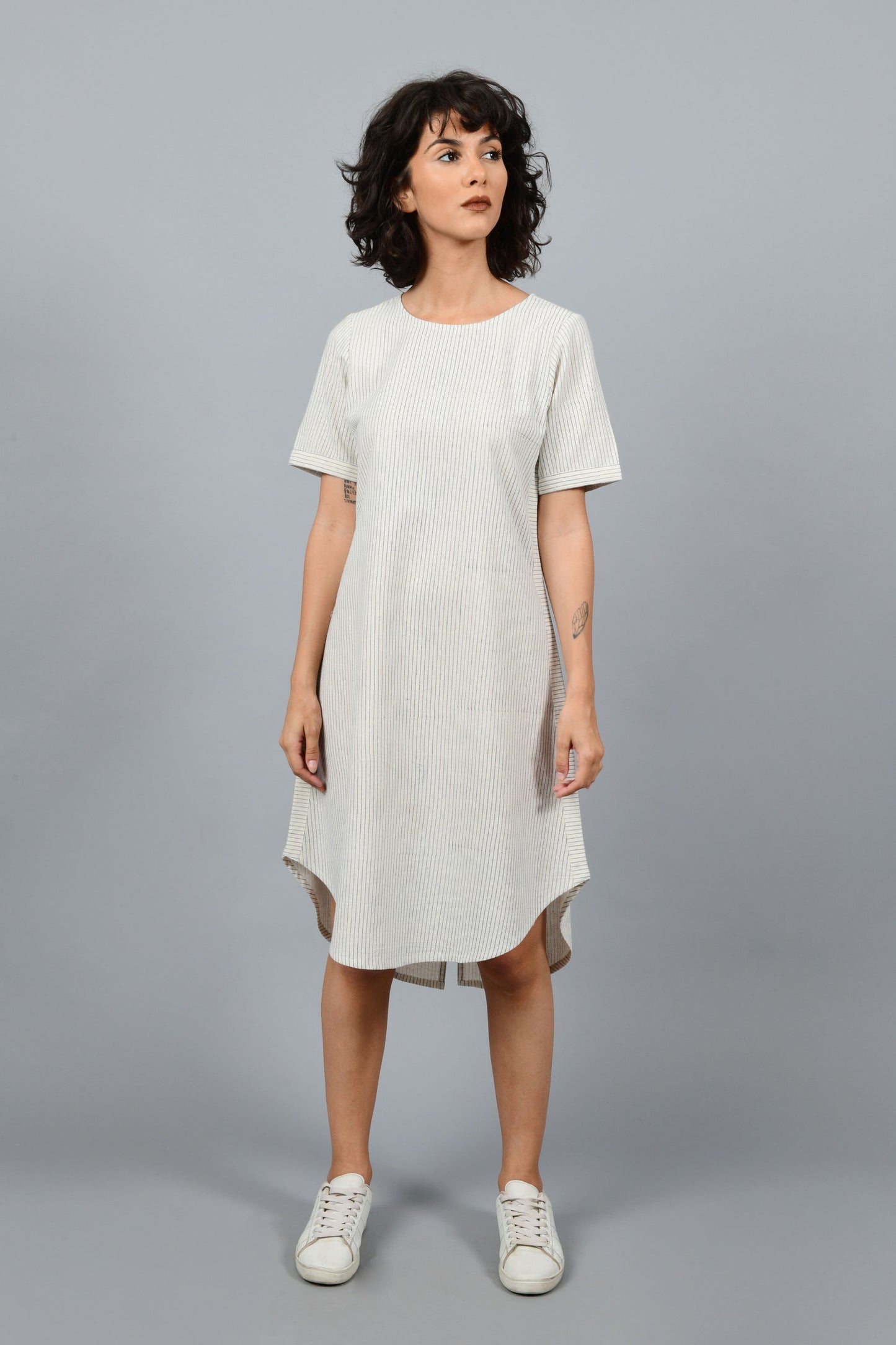 front of a female fashion model wearing minimally designed a-line round bottom western dress printed by Cotton Rack with blue stripes using brass block printing over handspun handwoven khadi cotton from maheshwar