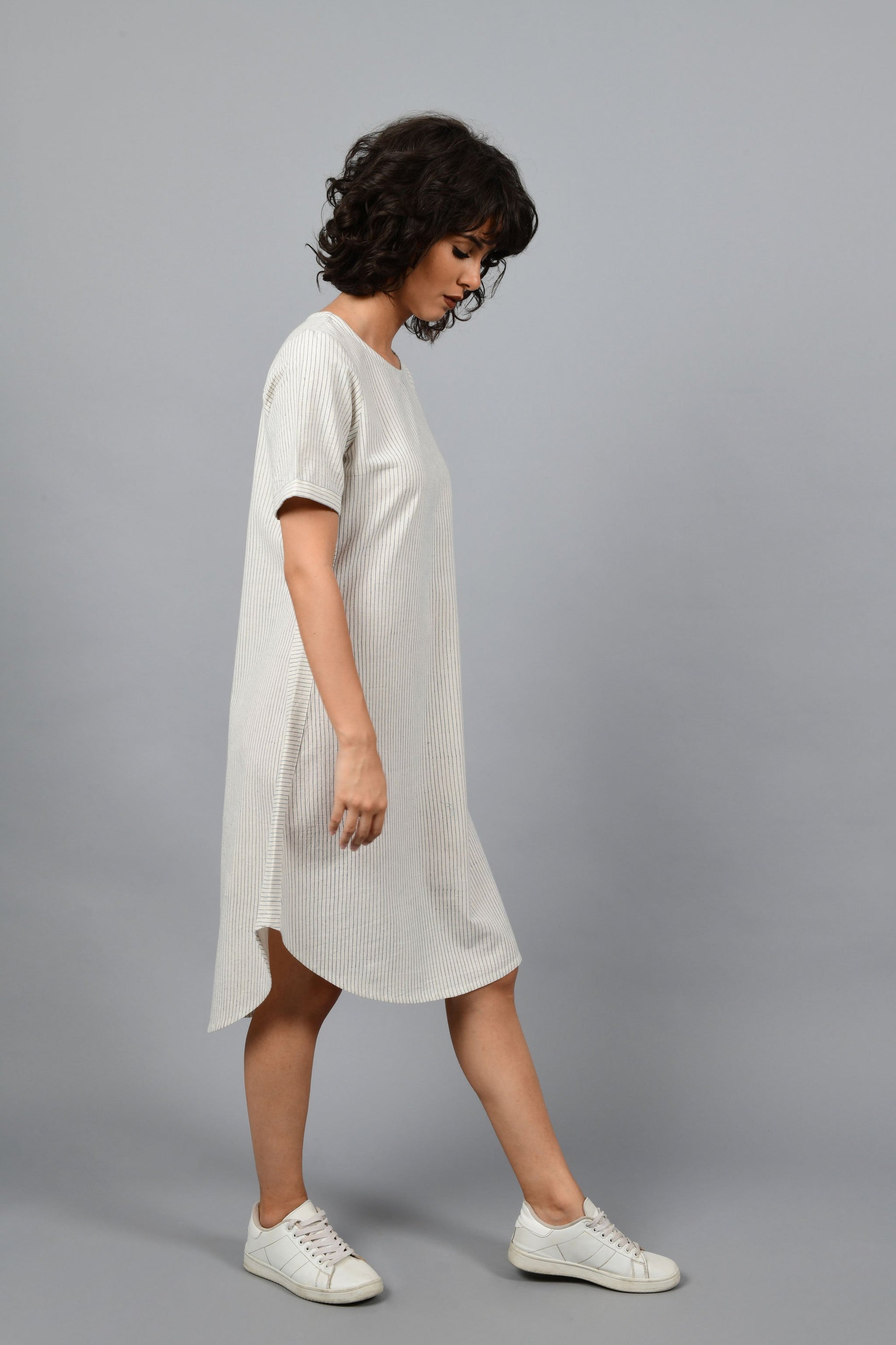 side pose of a womenswear fashion model wearing a minimally designed a-line round bottom western dress by Cotton Rack printed with blue stripes using brass block printing over handspun handwoven khadi cotton from maheshwar