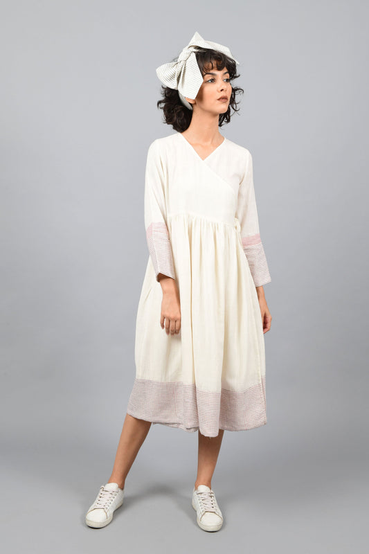 front of a model wearing an angrakha dress printed with red and blue check in the hem and sleeves using brass block printing over handspun handwoven khadi cotton from rajasthan. paired with head band tied as bow.