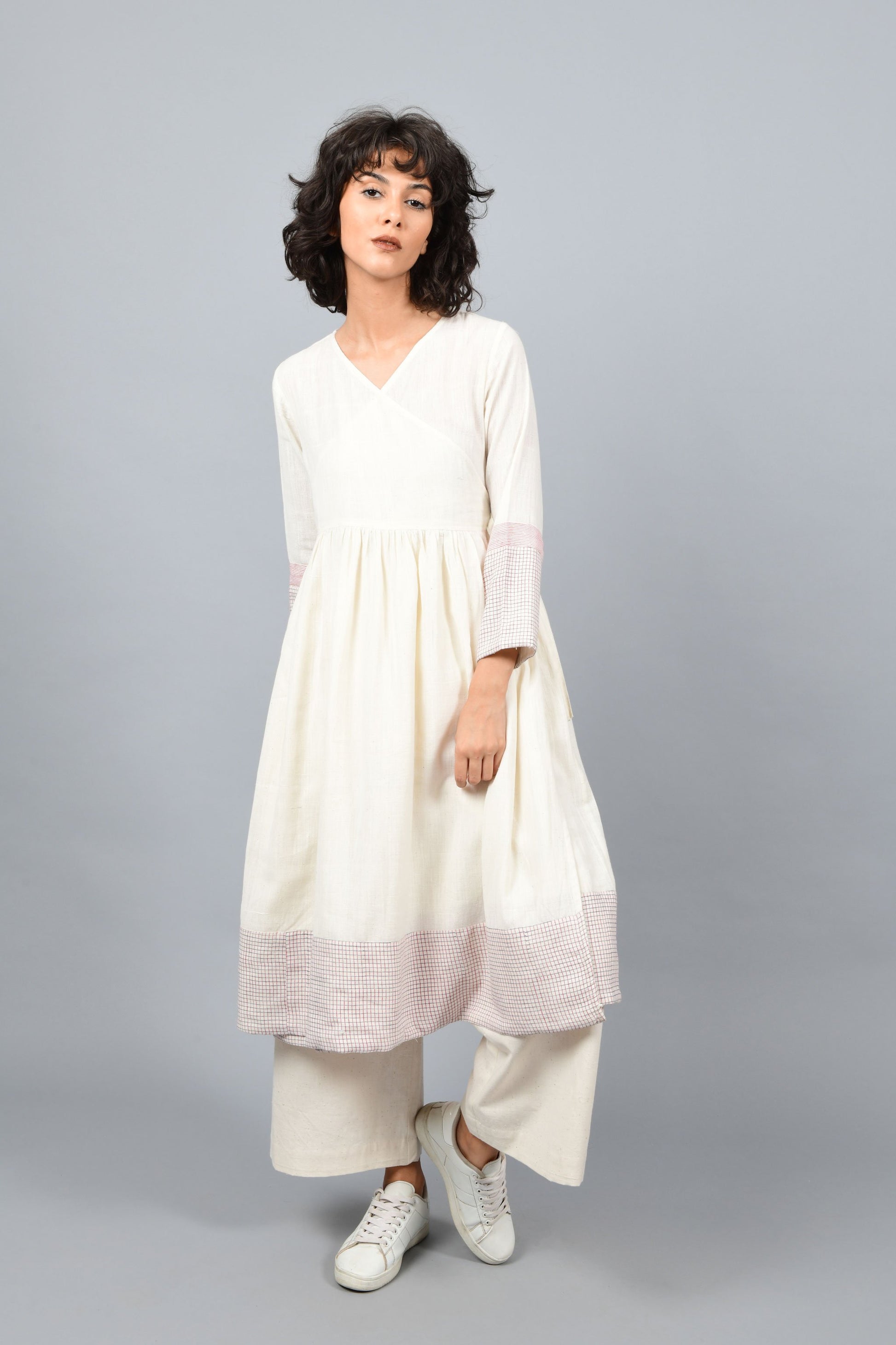 front of a model wearing an angrakha dress printed with red and blue check in the hem and sleeves using brass block printing over handspun handwoven khadi cotton from rajasthan. paired with off-white palazzos