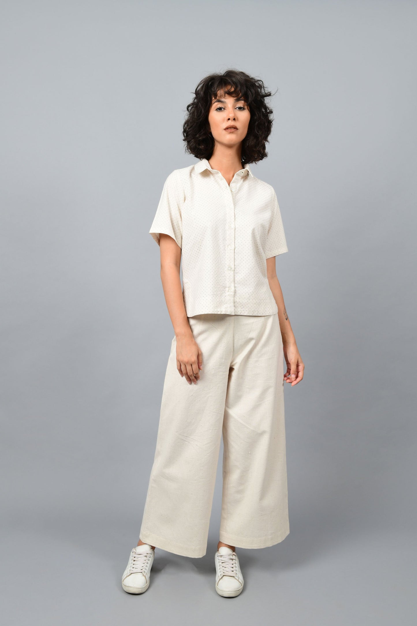 Model wearing off-white Khadi cotton relaxed shirt top printed with fine blue dots printed using metal block by Cotton Rack inspired by artist agnes martin. Posing straight for the camera.