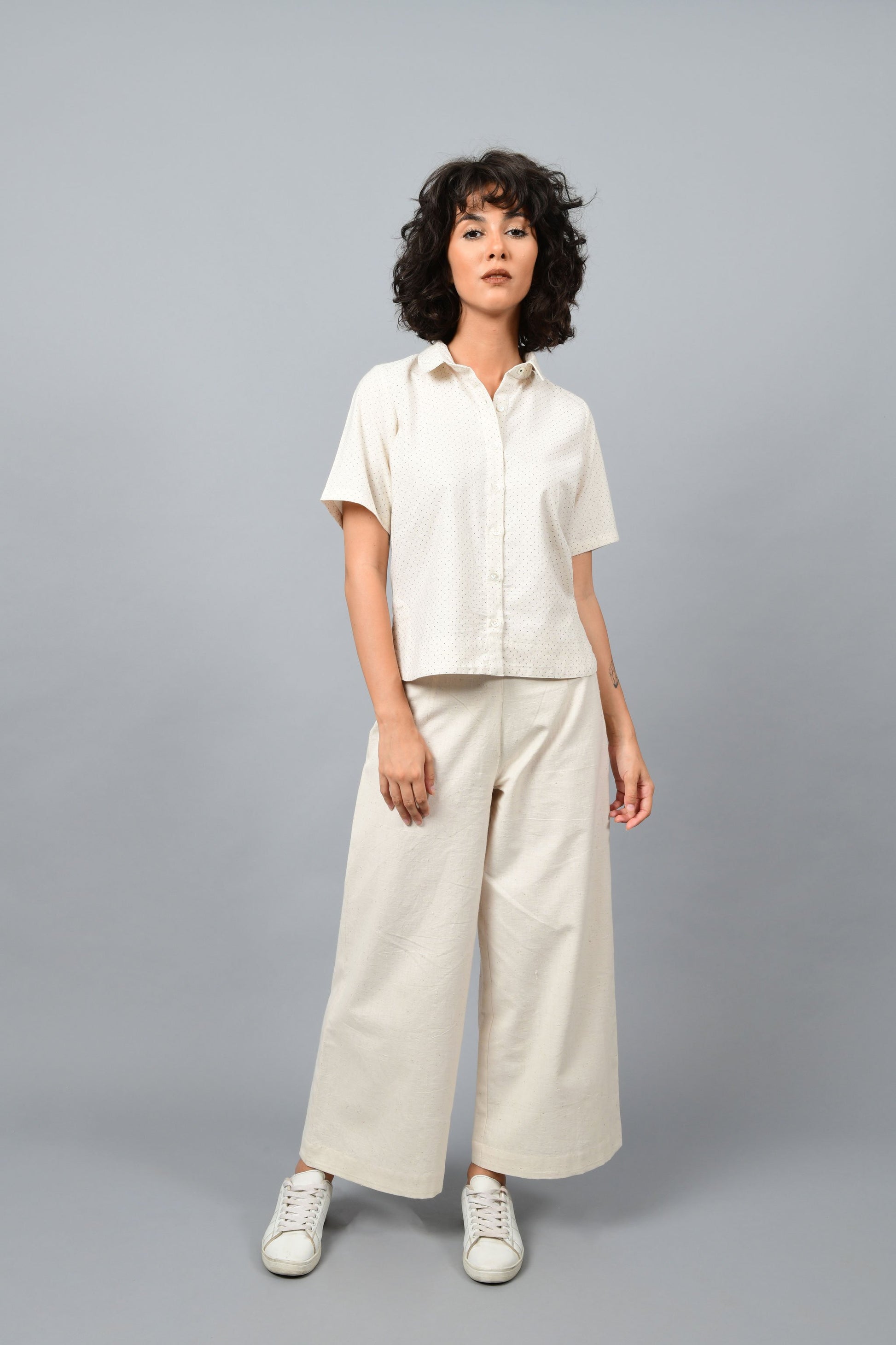 Model wearing off-white Khadi cotton relaxed shirt top printed with fine blue dots printed using metal block by Cotton Rack inspired by artist agnes martin. Posing straight for the camera.