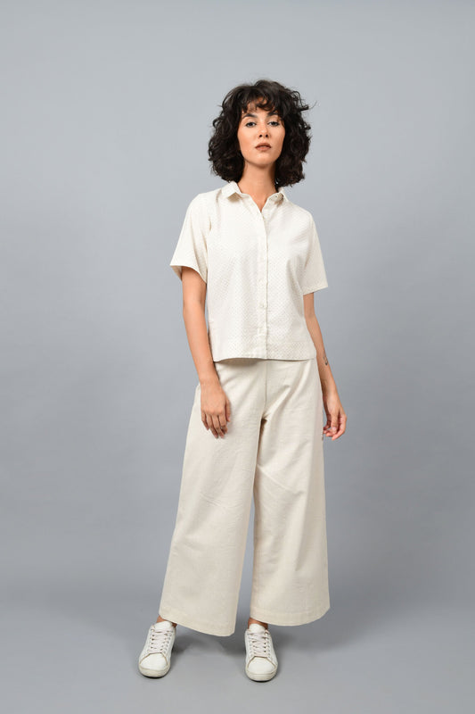 Model wearing off-white Khadi cotton relaxed shirt top printed with fine blue dots printed using metal block by Cotton Rack inspired by artist agnes martin. Posing straight for the camera.