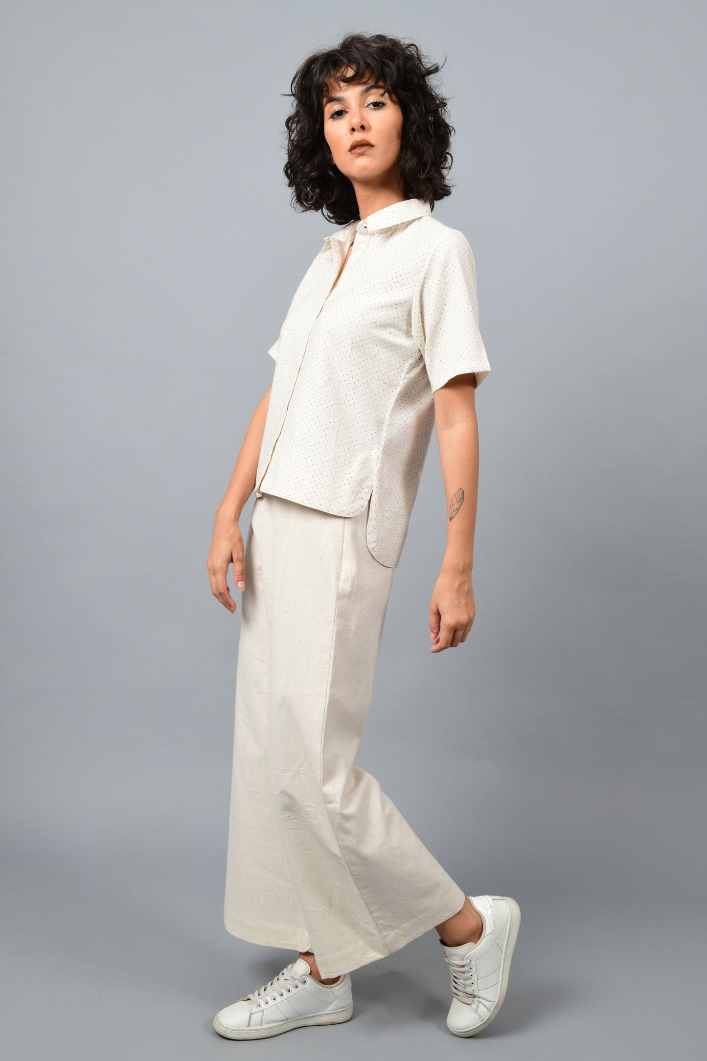 Model wearing off-white Khadi cotton relaxed shirt top printed with fine blue dots printed using metal block by Cotton Rack inspired by artist agnes martin. Posing facing left for the camera.