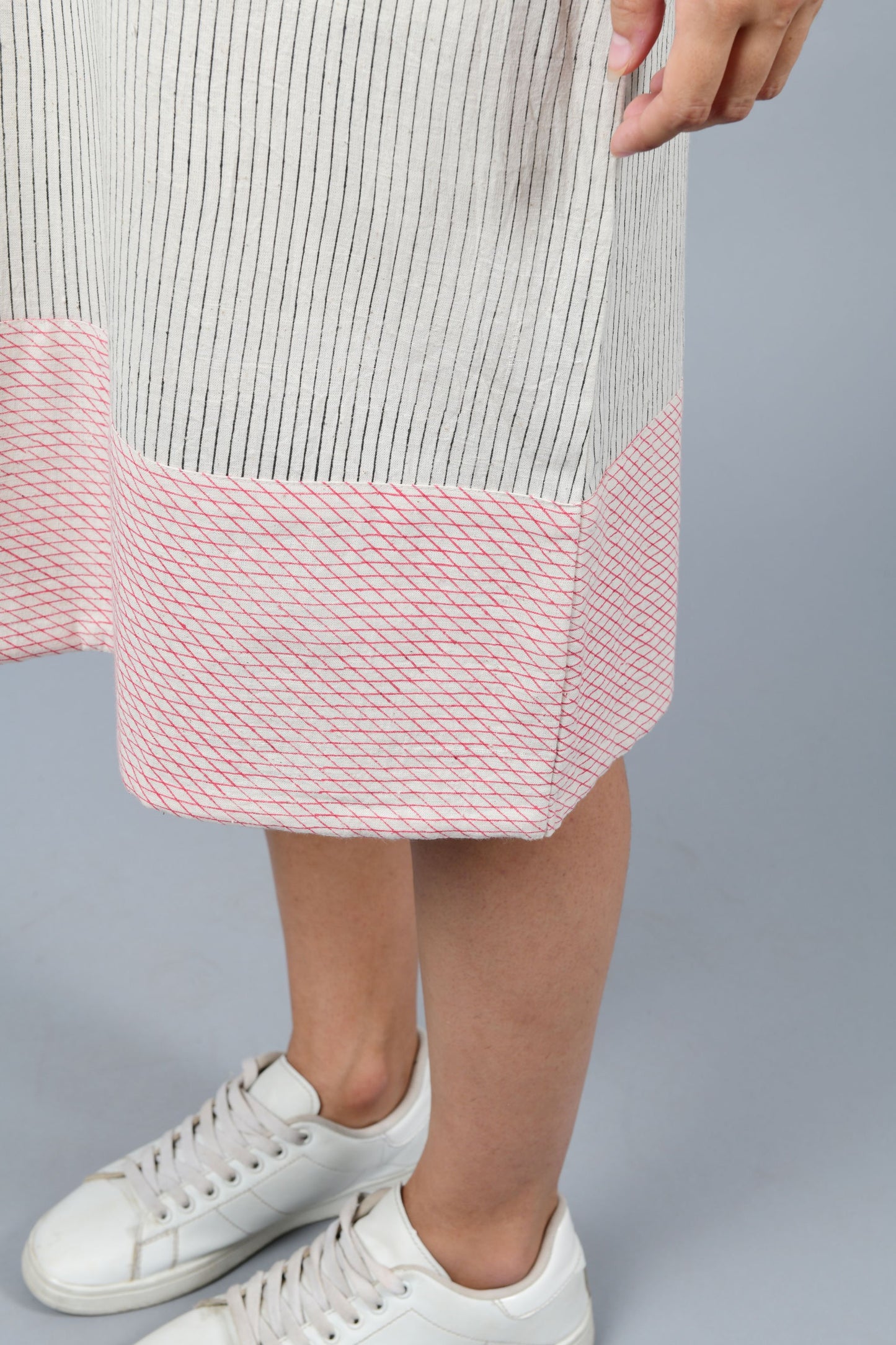 close-up of the hem details of the model wearing black block printed black pin stripes with red checks on the hem on off-white handspun and handwoven khadi cotton sleeveless dress.