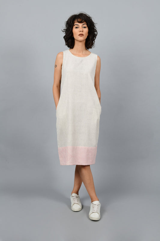 Model wearing black block printed black pin stripes with red checks on the hem on off-white handspun and handwoven khadi cotton sleeveless dress, posing straight for the camera.