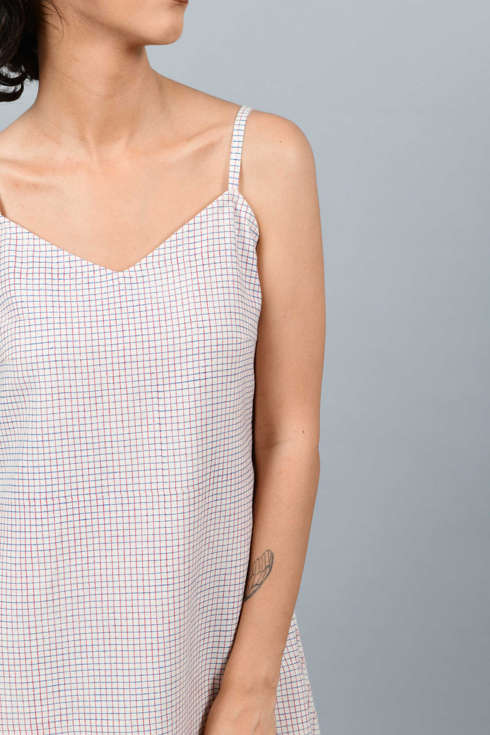 Close-Up of model wearing hand block printed handspun handwoven cotton khadi dress, printed with checks of red and blue on an off-white base. The model is also wearing an off-white printed bow in the same technique
