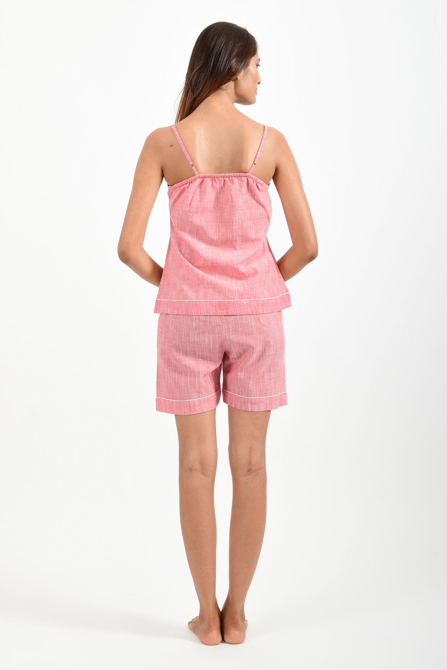 Back pose of an Indian female womenswear fashion model in azo-free space dyed pink handspun and handwoven khadi cotton spaghetti top and boxers by Cotton Rack.