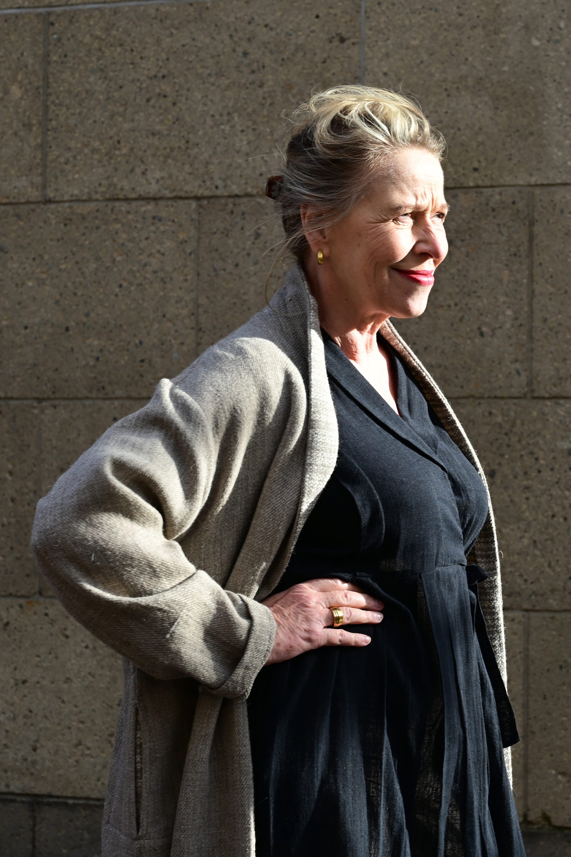 Close up of a middle aged european model posing wearing brown woolen long shrug with ivory woven pattern on the collar over a black wrap around dress. This shrug is made of handspun and handwoven Indian sheep wool by Cotton Rack.