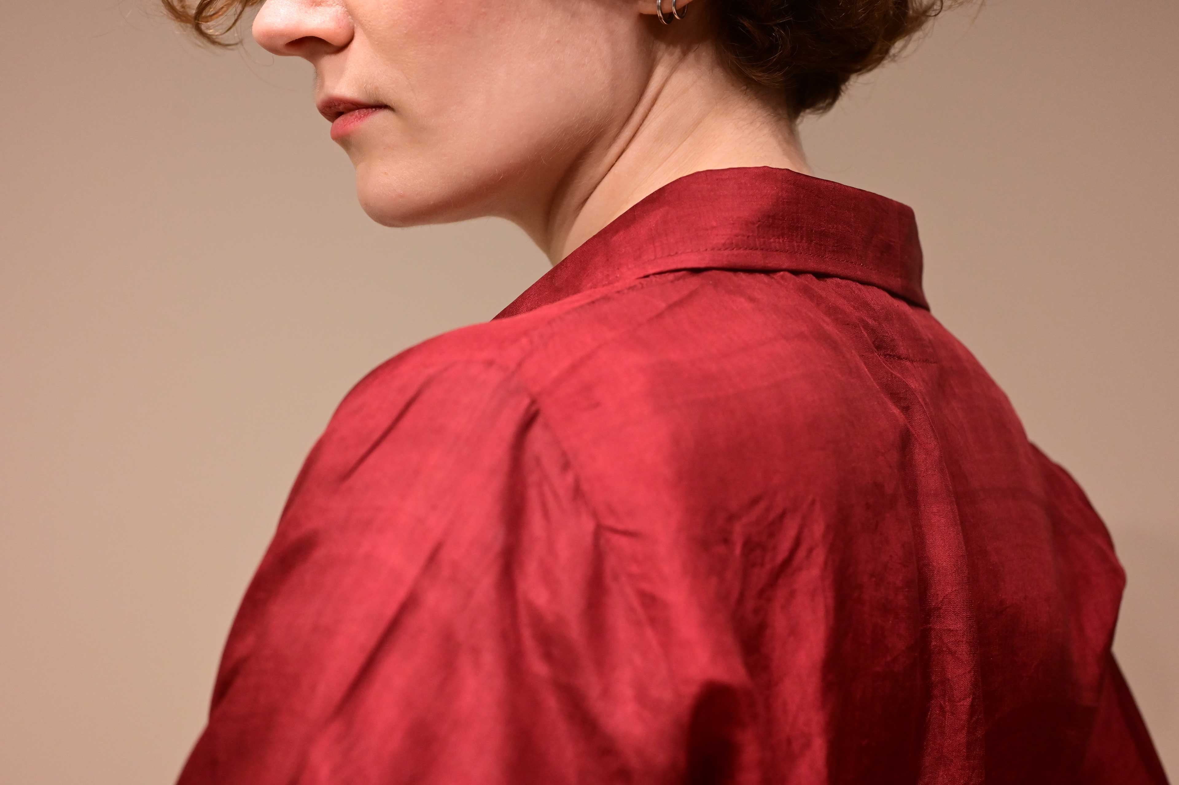 partial face and back of a european caucasian women wearing a red silk formal shirt.