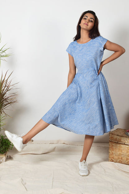 Indian girl with black hair and white sneakers wearing a blue a-line dress made with cotton that hand spun and hand woven.