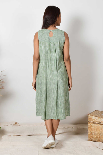 back of a dark haired Indian girl wearing a handspun cotton green sleeveless pleated dress.a