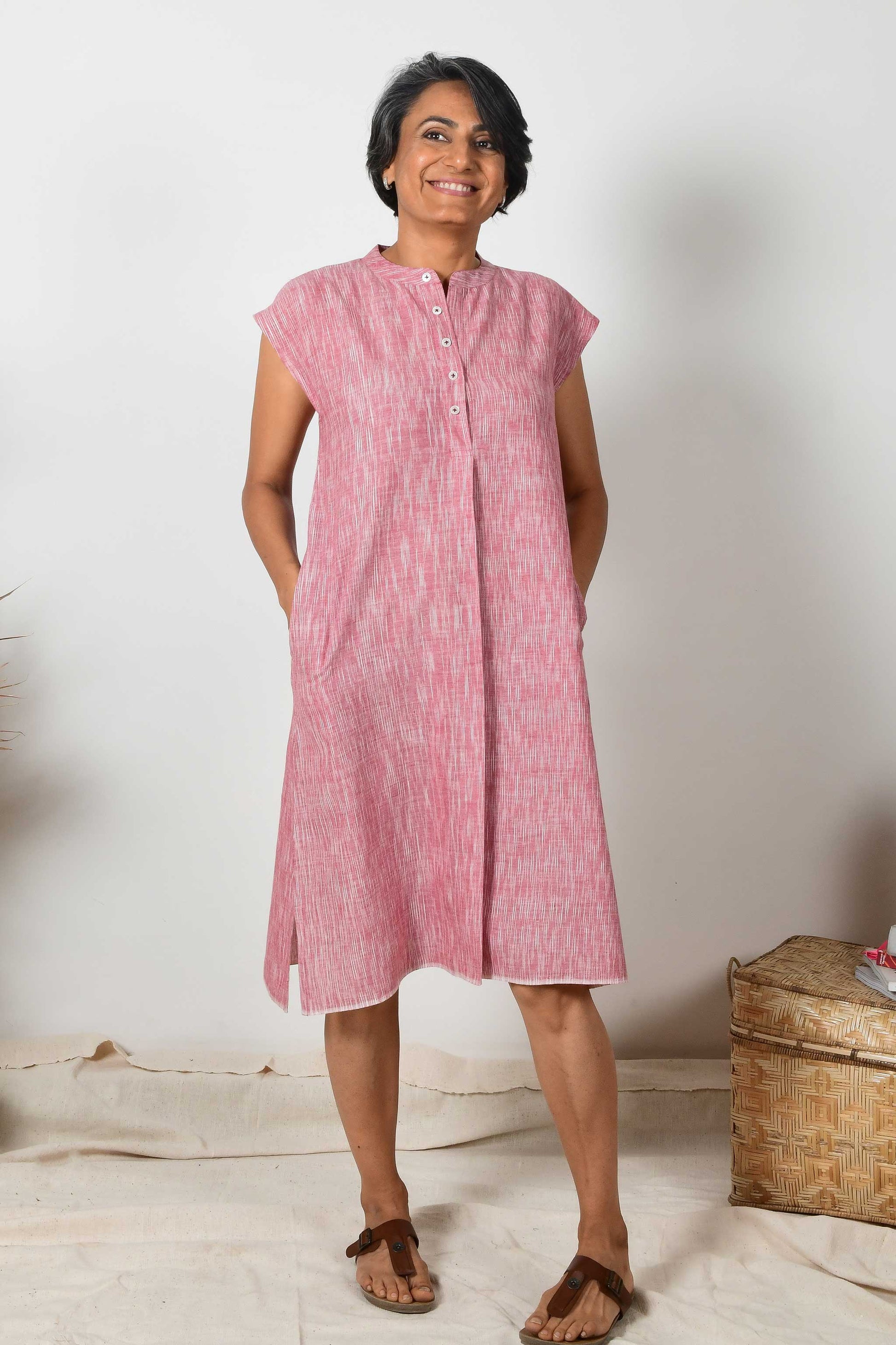 A smiling Indian woman wearing a short sleeved brick red cotton midi dress made with hand spun and hand woven natural fabric.