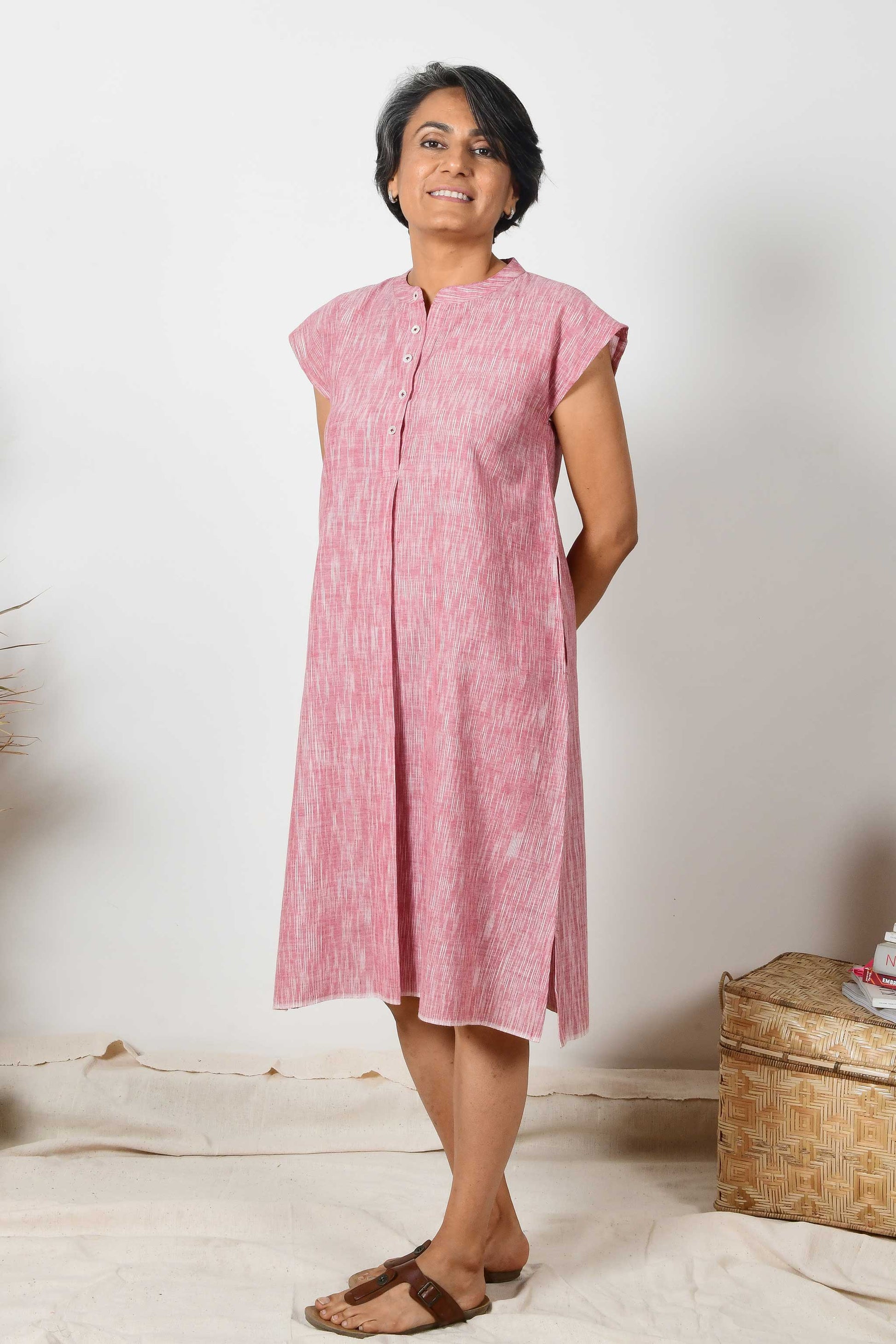 A smiling Indian woman wearing a short sleeved brick red cotton midi dress made with hand spun and hand woven natural fabric.