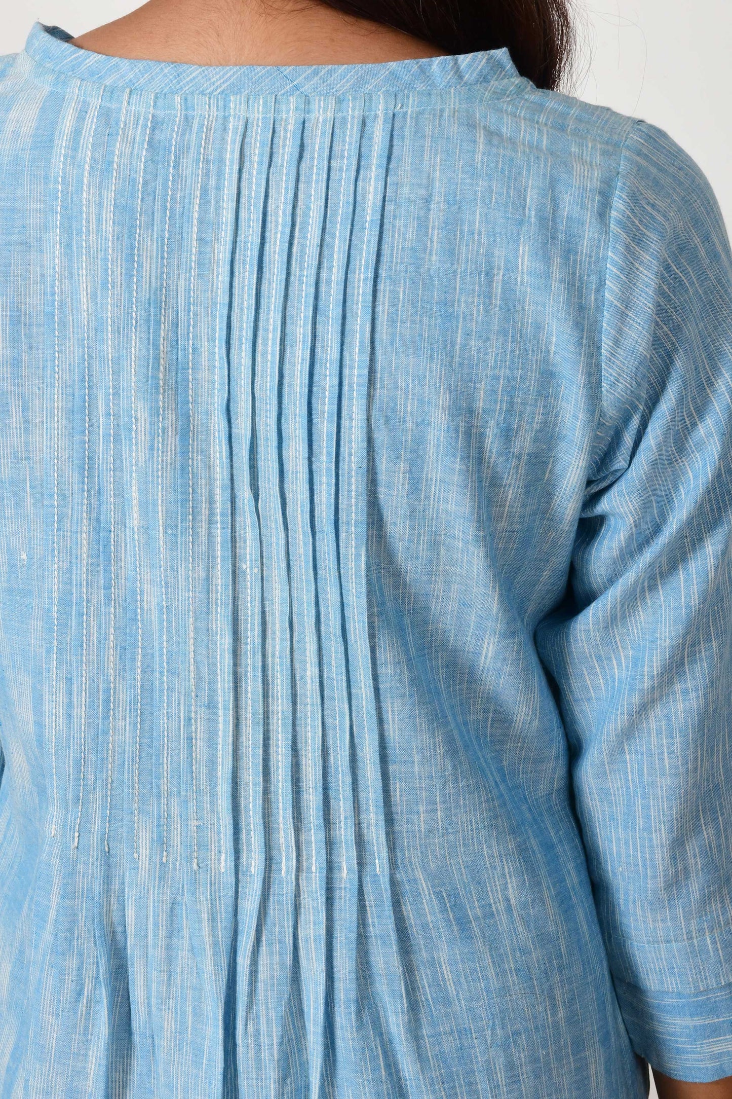 close up of knife pleats on the back of the blue textured cotton dress made of hand spun and hand woven cotton.