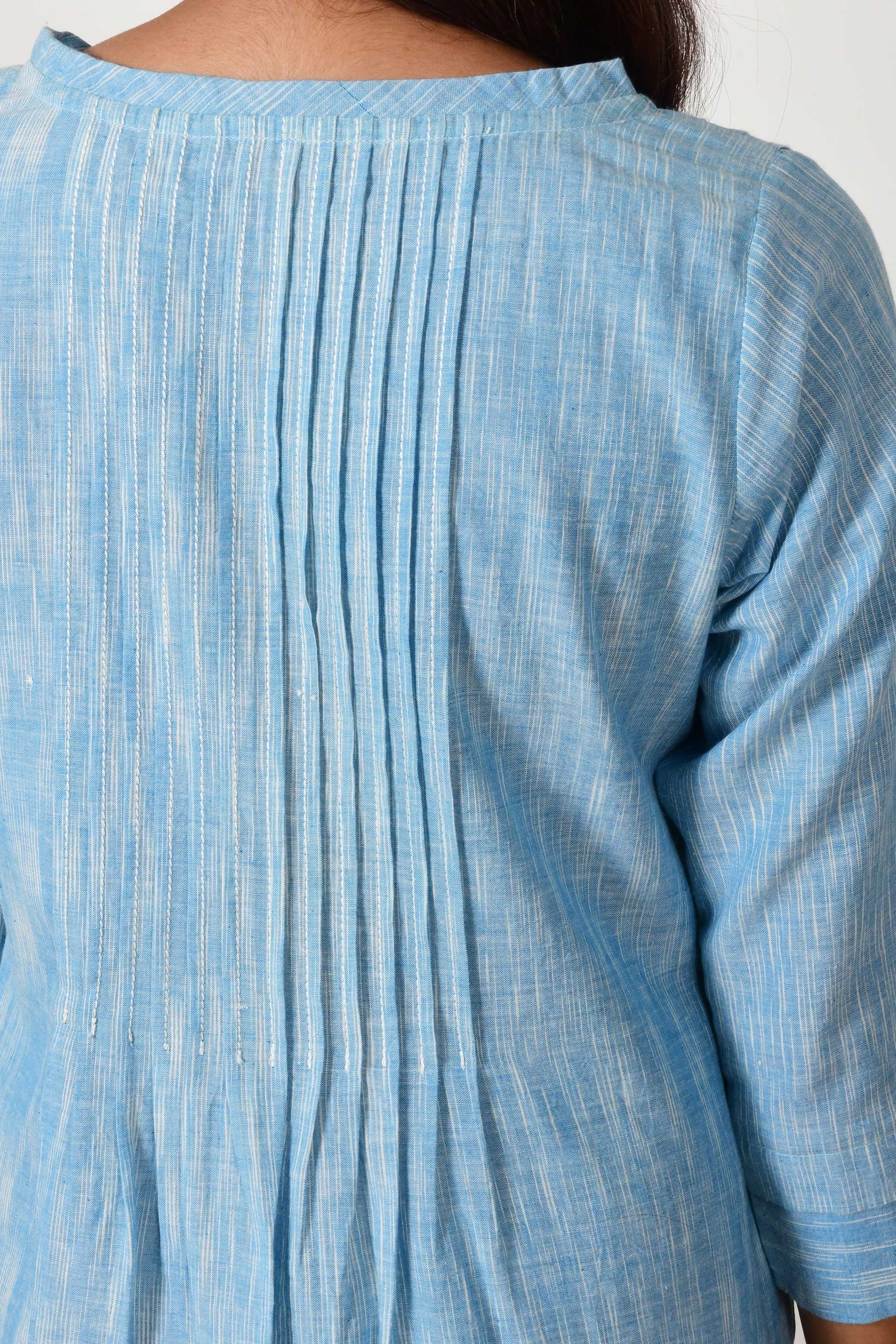 close up of knife pleats on the back of the blue textured cotton dress made of hand spun and hand woven cotton.
