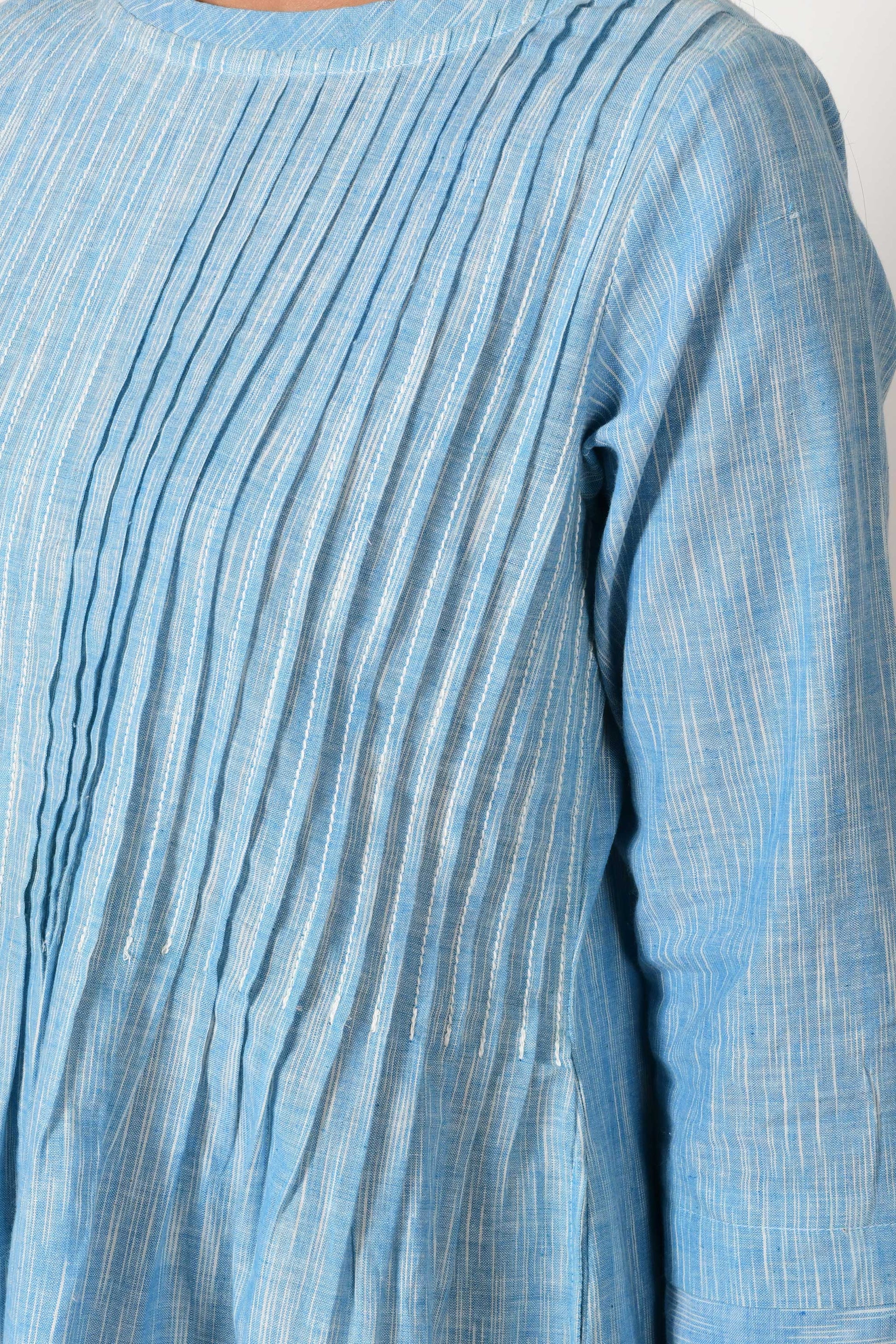 close up of knife pleats on the bust of the blue textured cotton dress made of hand spun and hand woven cotton.