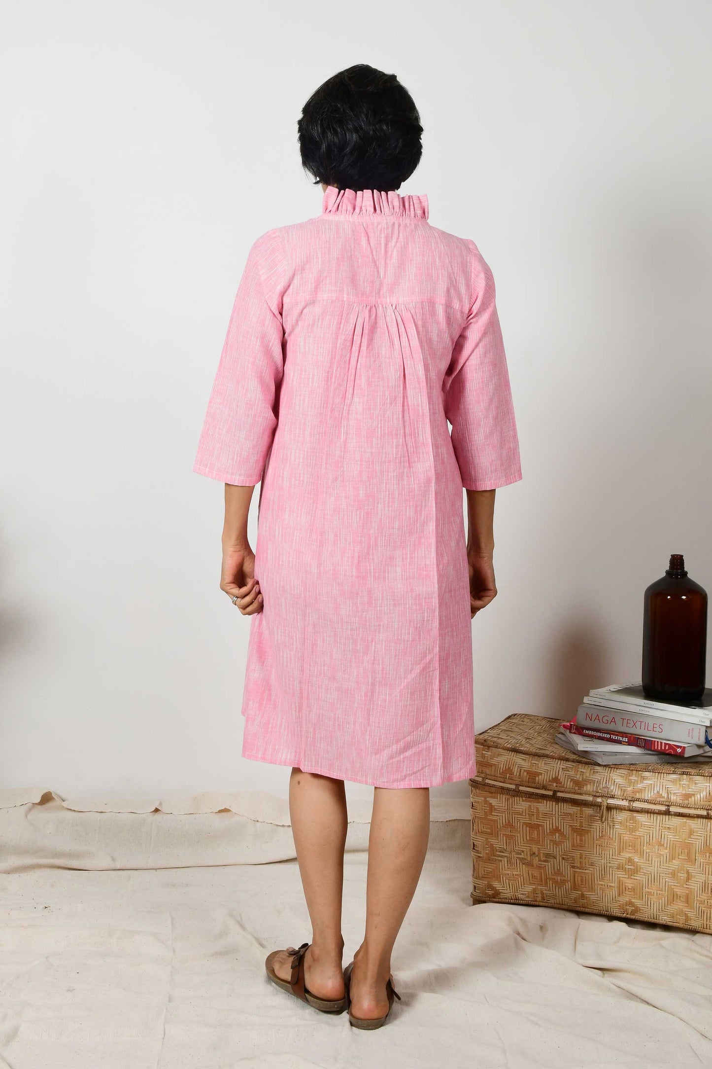 back of an indian fashion model wearing a pink kurta dress with flared neck and back yoke gather details.