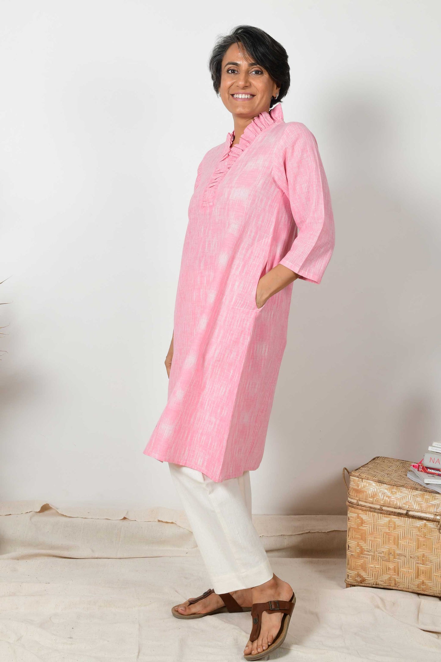 indian female model posing for the camera with hands in pockets and wearing white pants and pink flared neck dress kurta.